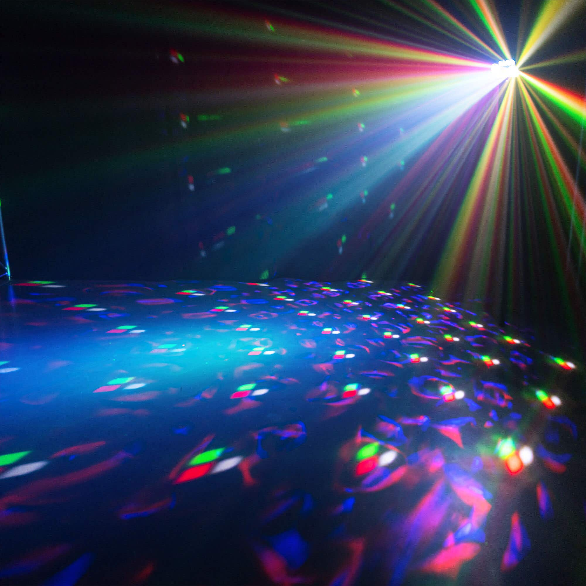 Un escenario con suelo azul refleja luces coloridas. Rayos de arcoíris brillan desde arriba. La escena sugiere ambiente de fiesta.