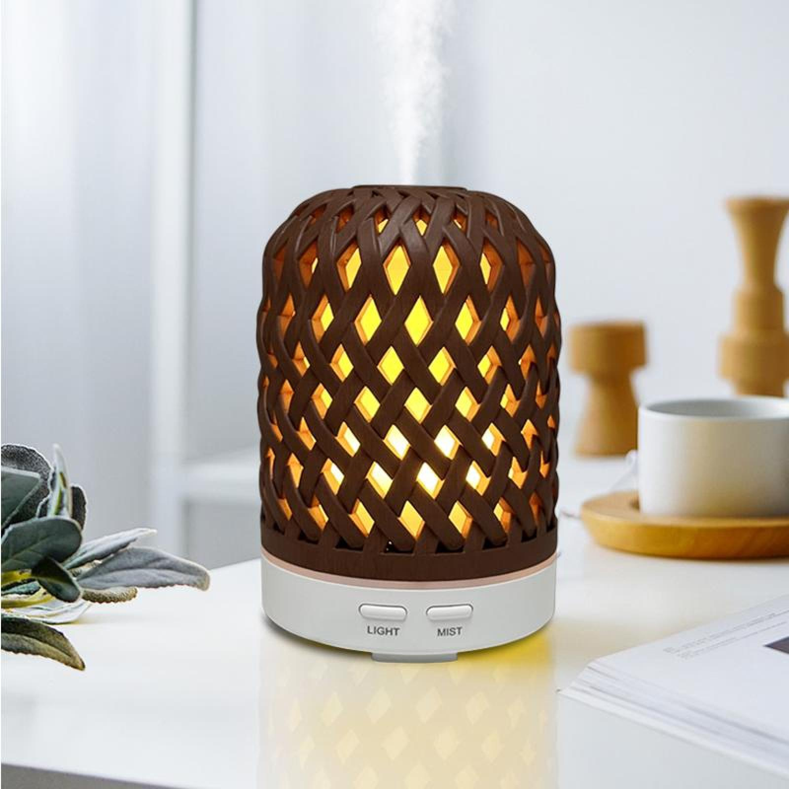 Ein brauner gewebter Diffusor mit gelbem Licht. Weiße Basis mit 'Light'- und 'Mist'-Tasten. Eine Pflanze und eine Tasse im Hintergrund.