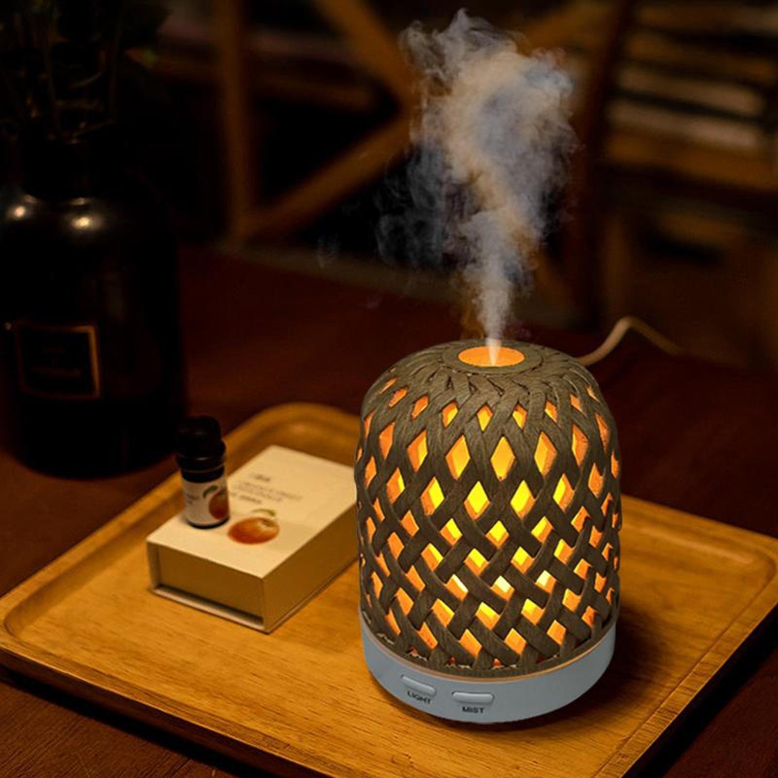 Ein beleuchteter Aroma-Diffusor mit gewebtem Design, der Dampf abgibt. Weitere Artikel sind eine Flasche und ein Buch auf einem Holztablett.