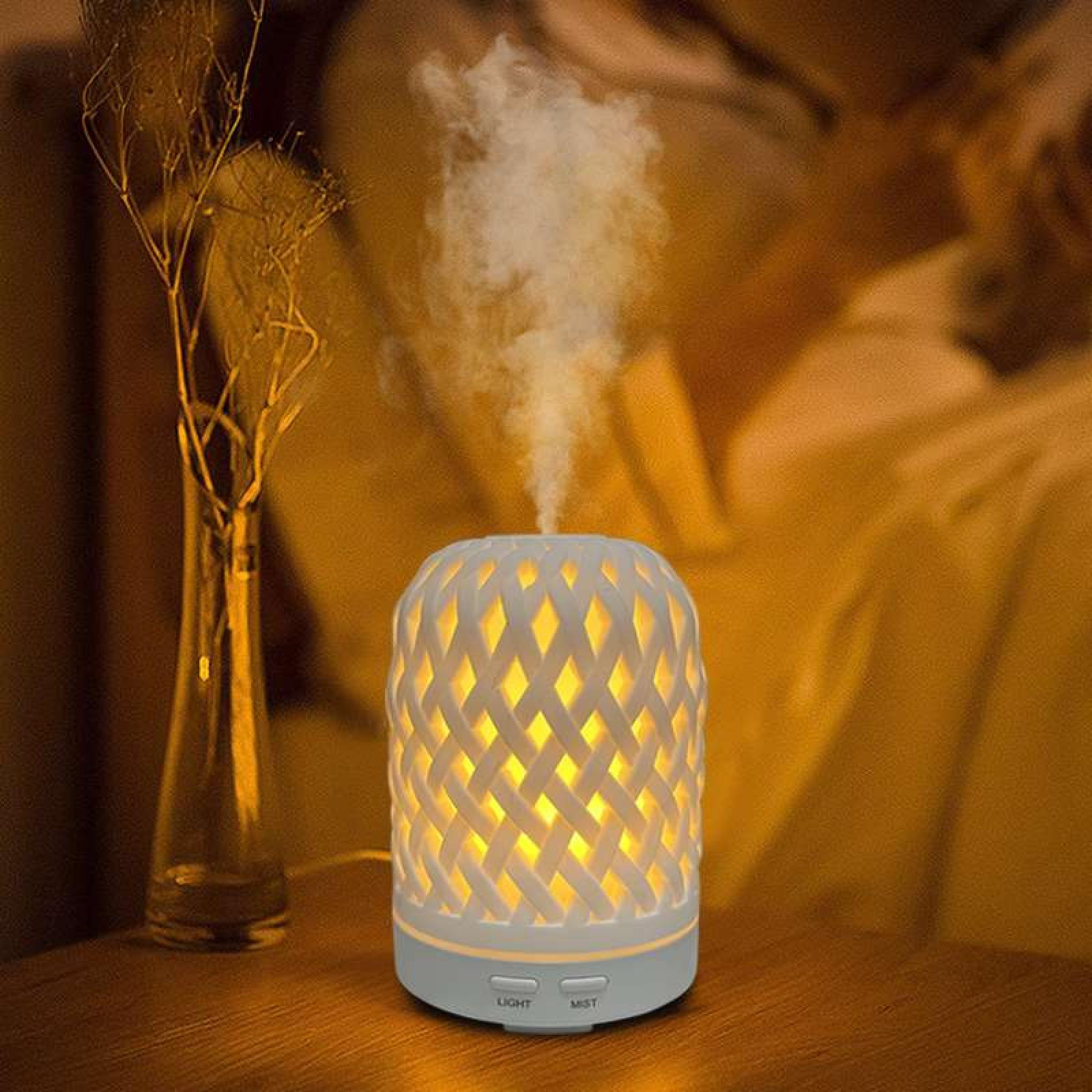 Ein weißer Diffusor verströmt Nebel. Links steht eine Vase mit Zweigen. Der Hintergrund ist ein warm getönter Stoff.