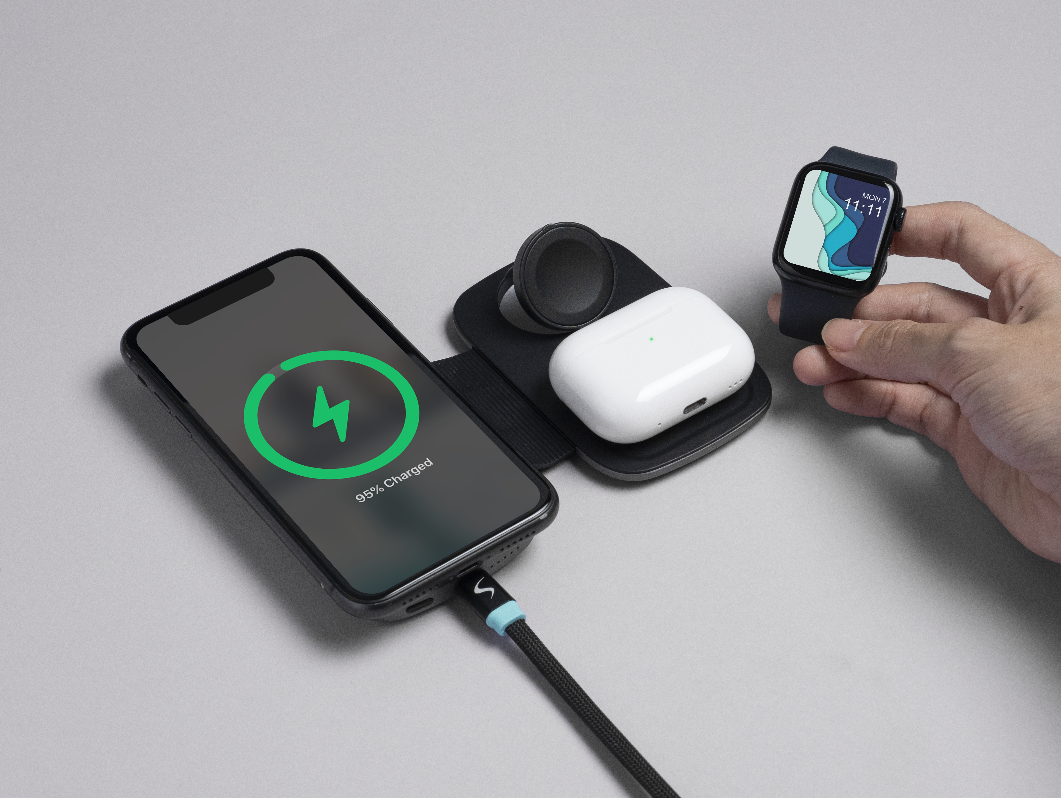 Telefon lädt mit 95 %, AirPods, Uhr, alles auf grauem Untergrund. Hand hält Uhr.
