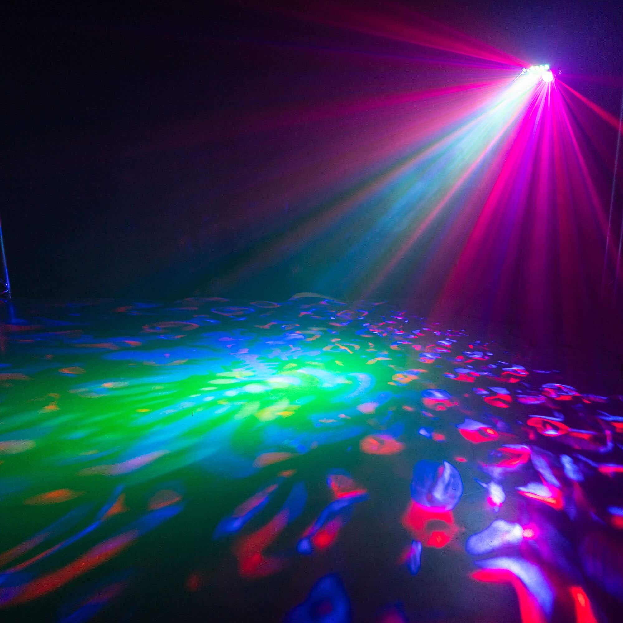 Un escenario iluminado con luces rosas, azules y verdes vibrantes. Las luces crean patrones en el suelo.