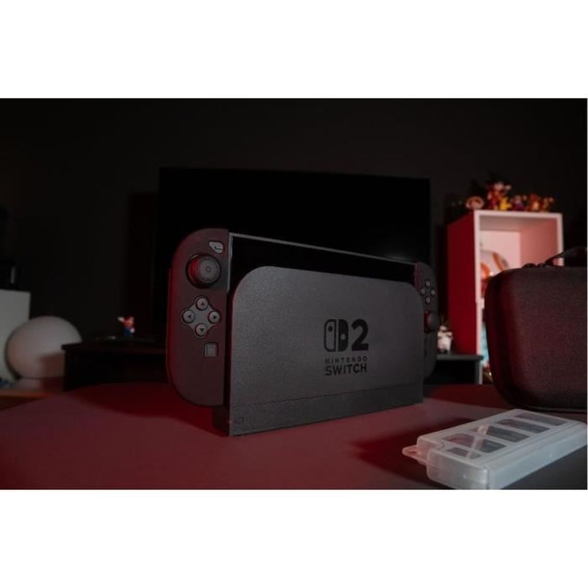 Een Nintendo Switch-console staat op een rood oppervlak. Een doorzichtige hoes en een draagtas bevinden zich rechts. Donkere achtergrond.