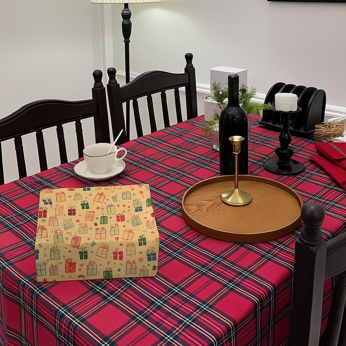 Ein Tisch mit einer rot karierten Tischdecke. Enthält eine Geschenkbox, eine Tasse, einen Kerzenhalter, eine Weinflasche und ein Tablett.