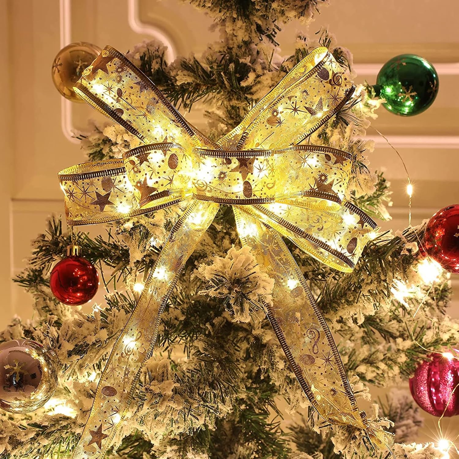 Ein geschmückter Weihnachtsbaum mit einer großen goldenen Schleife, Ornamenten und Lichtern. Die Schleife hat Sternmuster. Ornamente sind rot, grün und gold.