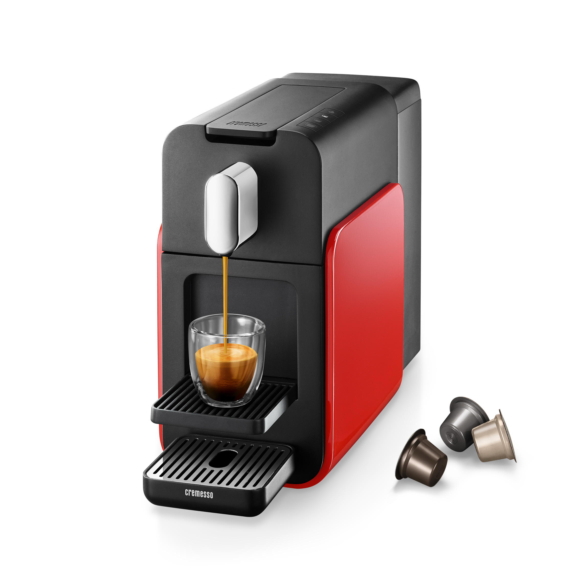 Eine rot-schwarze Kaffeemaschine brüht Kaffee in ein Glas. Drei Kapseln liegen in der Nähe.
