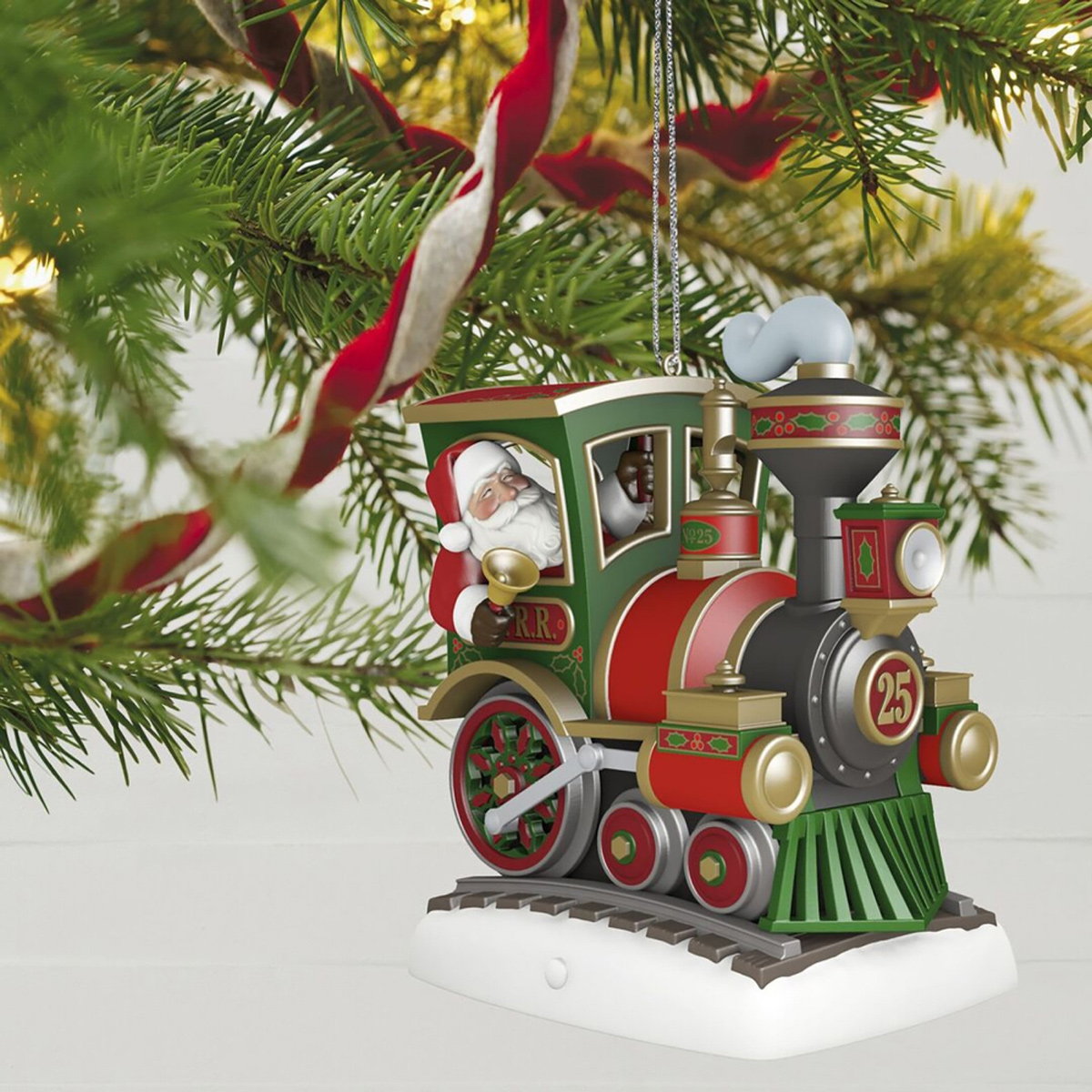 Ein Weihnachtszug-Ornament mit dem Weihnachtsmann im Inneren. Es hängt an einem Weihnachtsbaum mit rot-weißen Bändern.