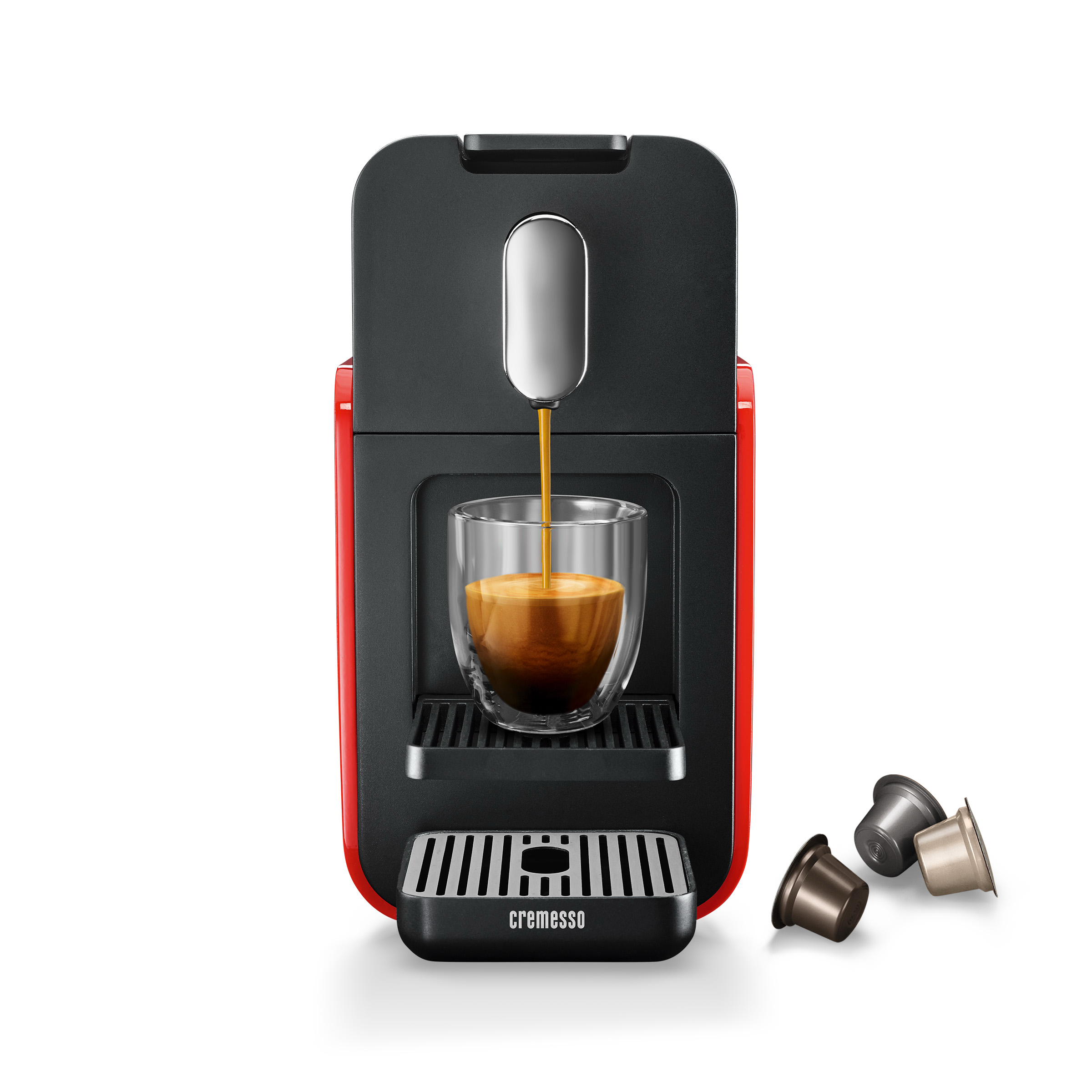 Rote und schwarze Kaffeemaschine gießt Kaffee in ein Glas. Kaffeepads sind auf weißem Hintergrund verstreut.