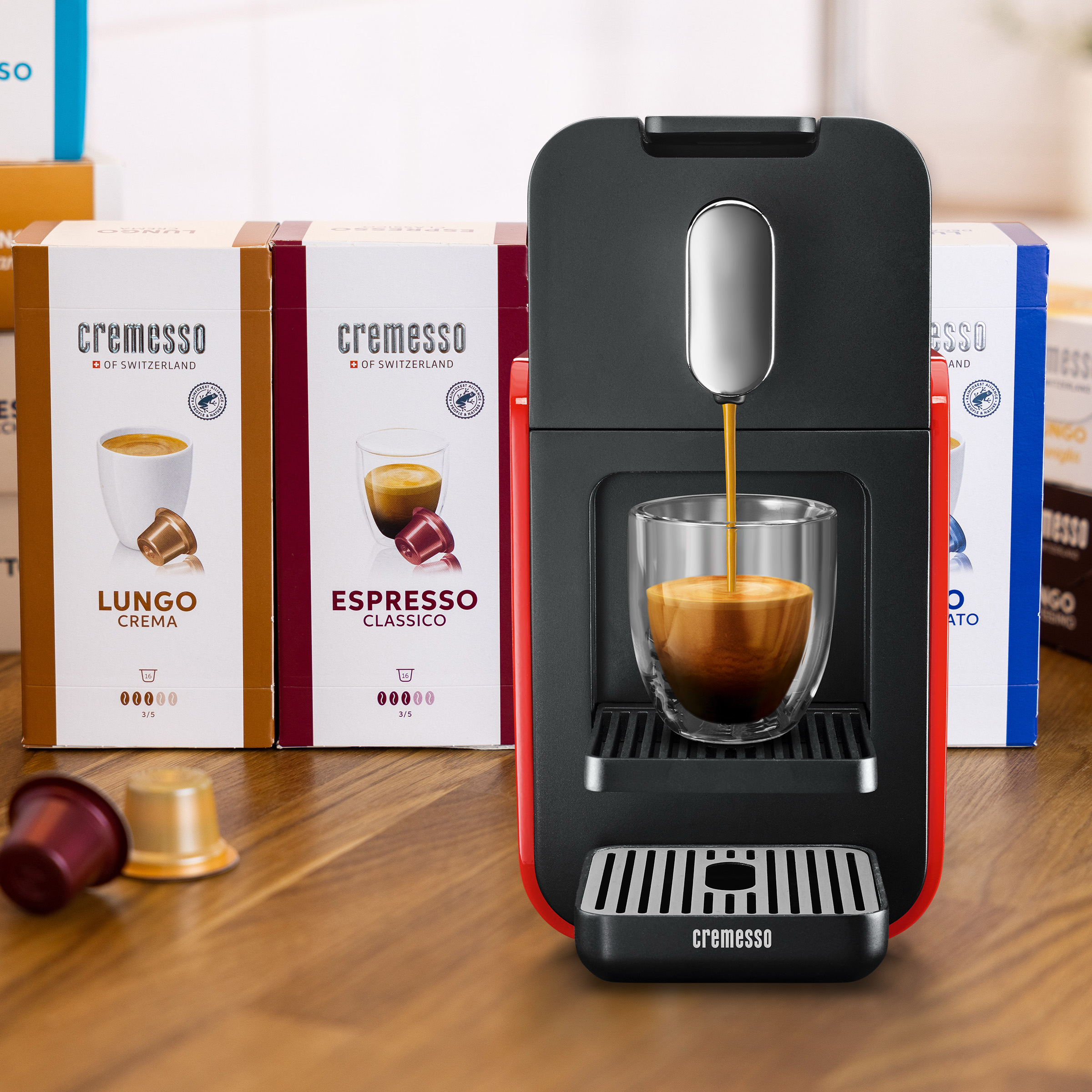 Kaffeemaschine mit Kaffee, der in ein Glas gegossen wird. Kapselpackungen im Hintergrund. Kapseln liegen auf dem Tisch.