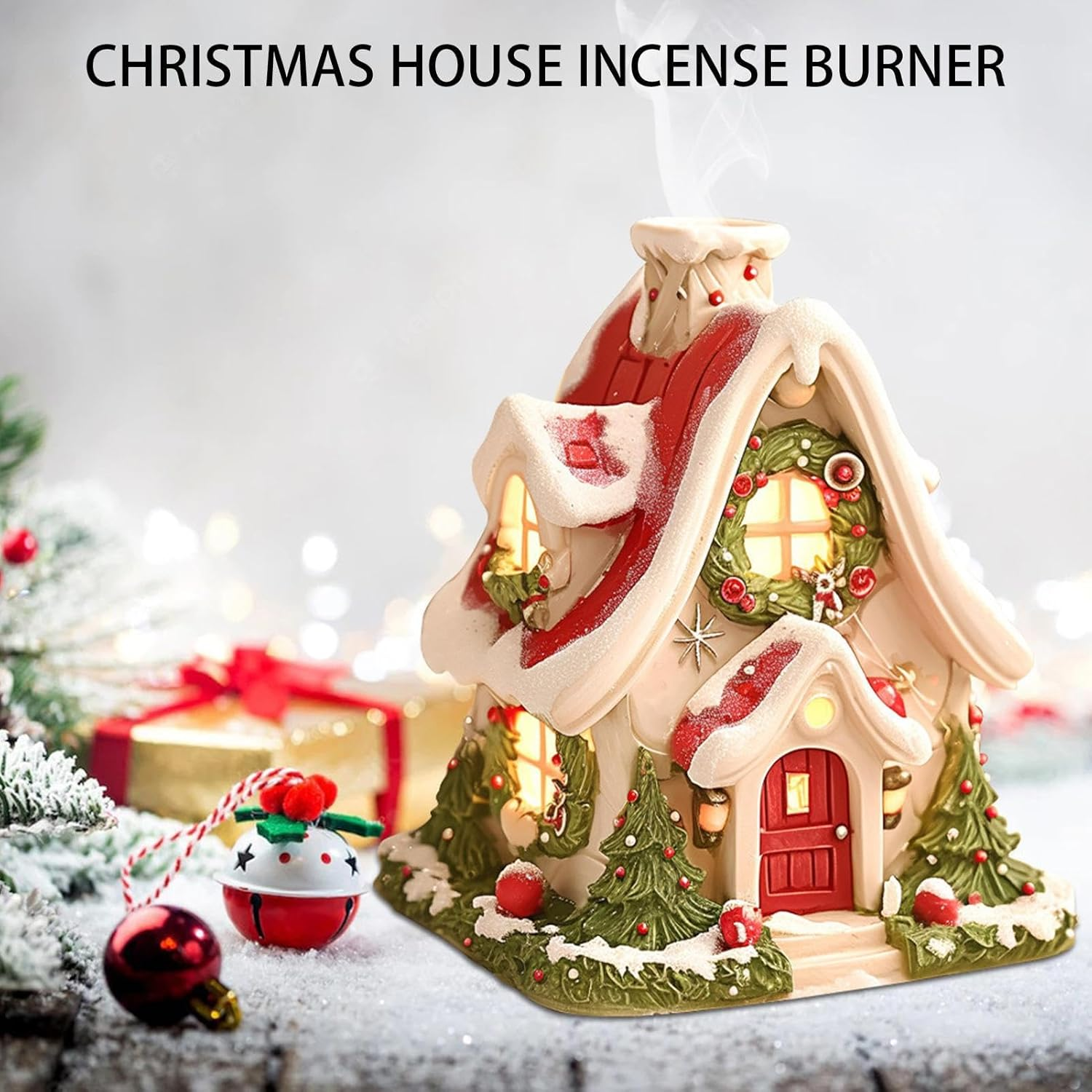 Ein Weihnachts-Haus-Räuchergefäß mit roter Tür, Kranz und schneebedecktem Dach. Eine Glocke, ein Ornament und Geschenke sind im Vordergrund.