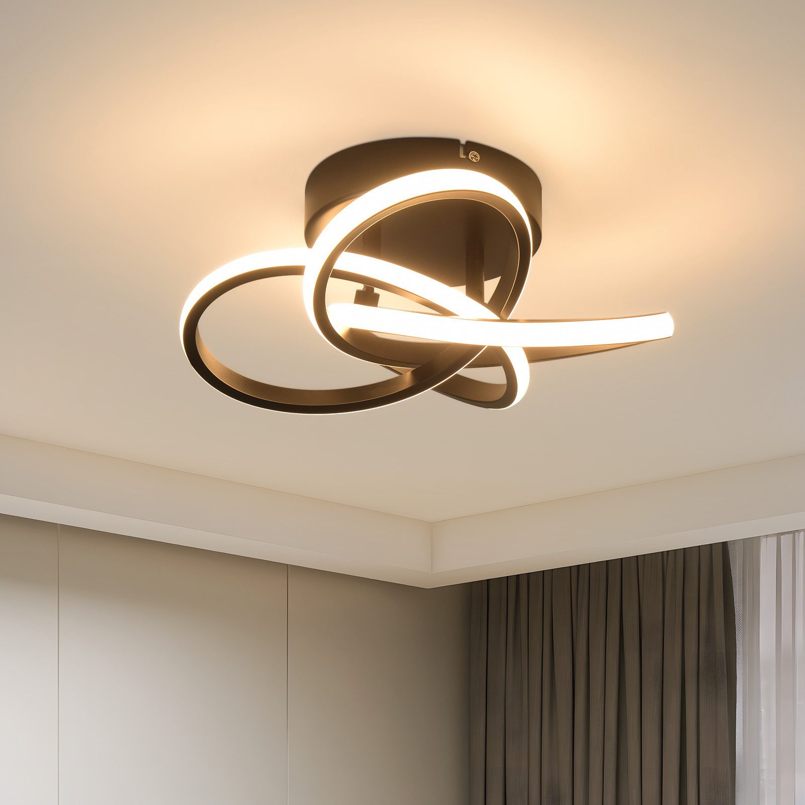 Lampada da soffitto con archi intrecciati e illuminati. Il soffitto è bianco, sotto un muro beige e una tenda scura.