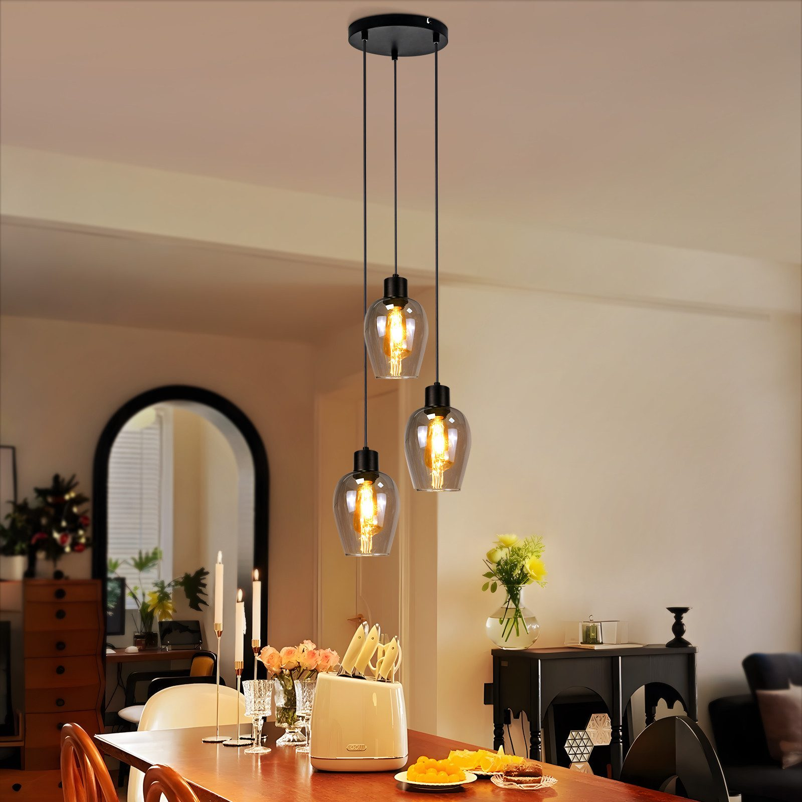 Sala da pranzo con tre lampade a sospensione. Tavolo apparecchiato con cibo, fiori e candele. Specchio e mobile sullo sfondo.