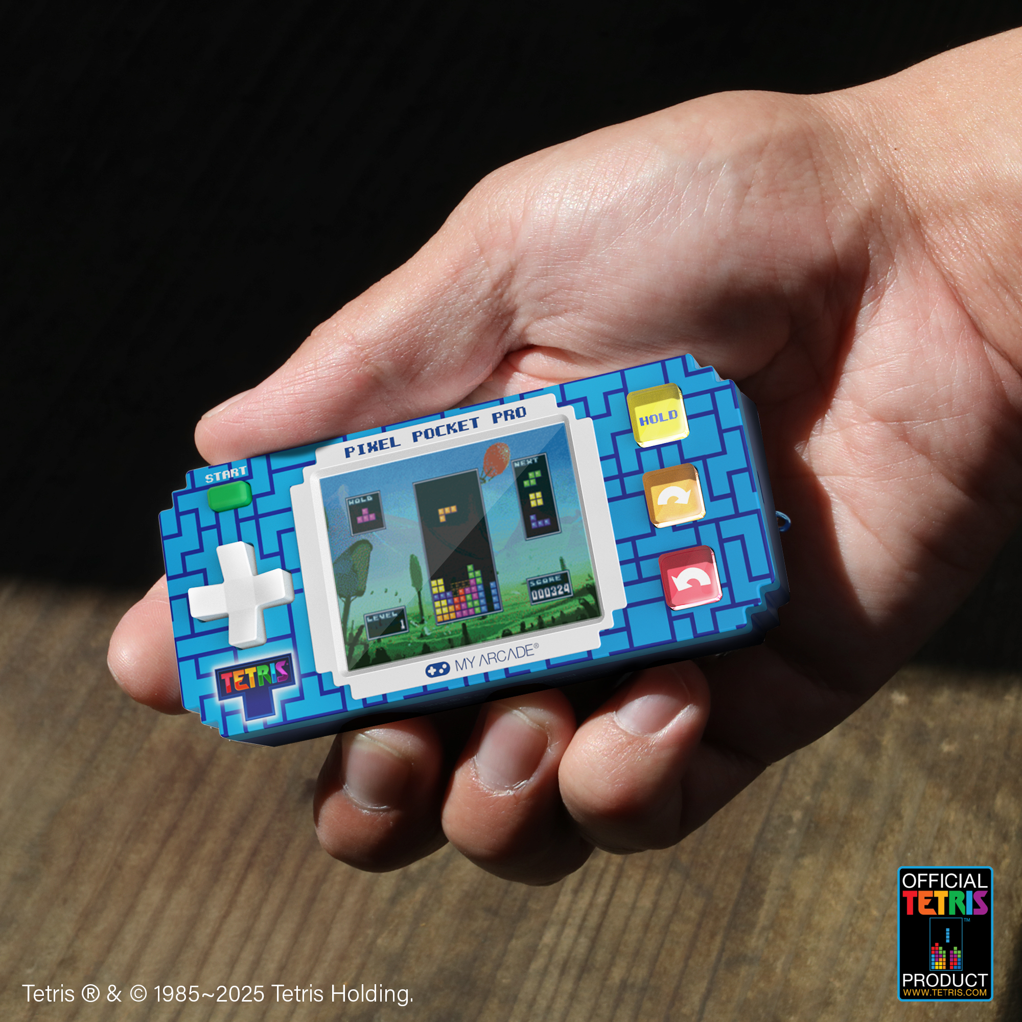 Una mano tiene in mano una console di gioco Tetris blu. Lo schermo mostra un gioco e i pulsanti sono visibili. Lo sfondo è scuro.