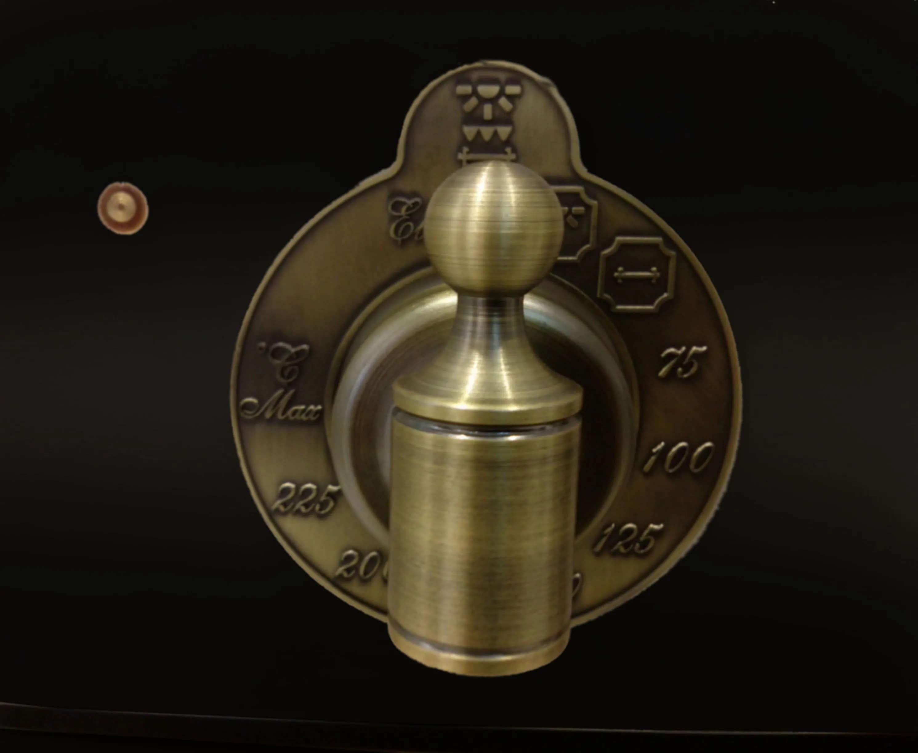 Ein Messing-Ofenknopf mit Temperaturmarkierungen auf schwarzem Hintergrund. Der Knopf hat eine runde Oberseite und einen zylindrischen Sockel.
