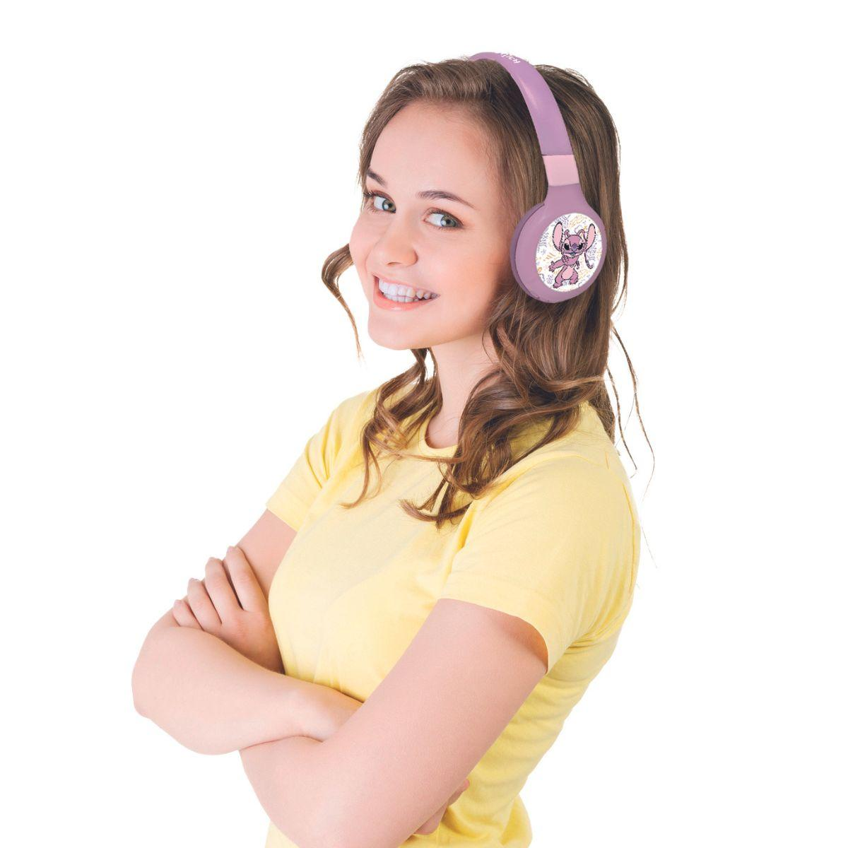 Una donna sorridente con cuffie viola con Stitch. Indossa una camicia gialla, con le braccia incrociate, su sfondo bianco.