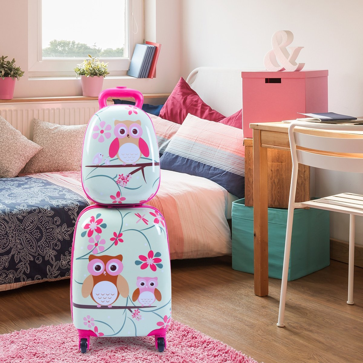 Dos maletas con temática de búho apiladas sobre una alfombra rosa. Habitación con cama, escritorio y ventana.