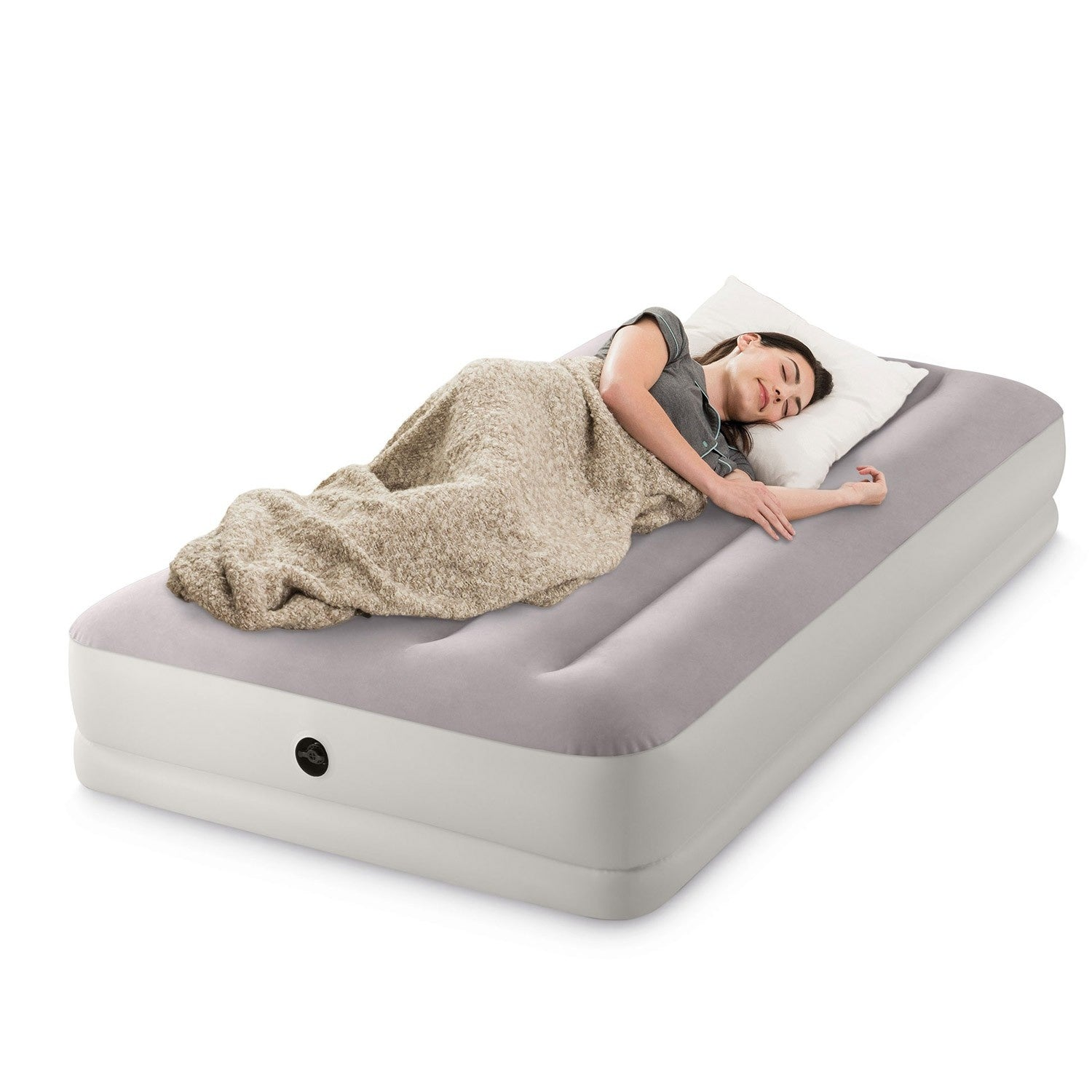 Una mujer duerme en un colchón de aire gris con una almohada blanca y una manta beige, aislado sobre fondo blanco.