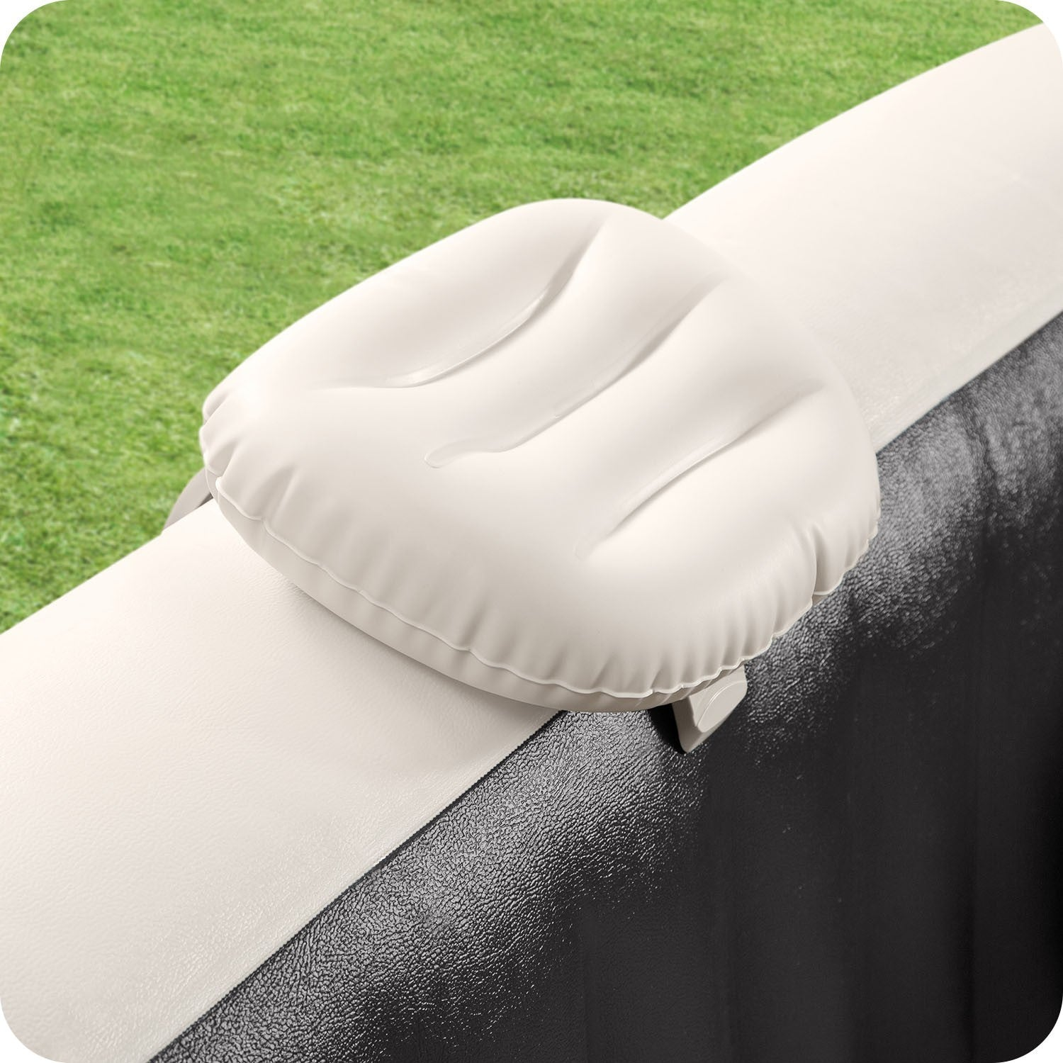 Una almohada inflable blanca sujeta al borde de un spa. Hierba verde al fondo. El borde del spa es blanco y negro.