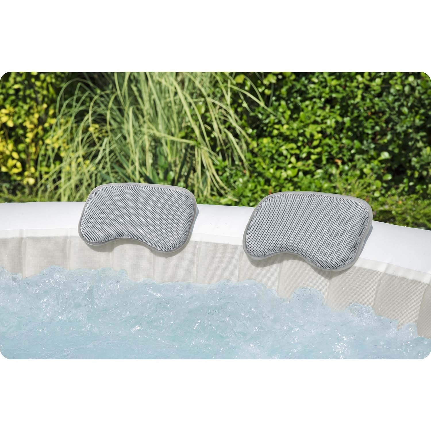 Dos reposacabezas grises en un jacuzzi. Agua burbujeante en primer plano, arbustos verdes en el fondo.
