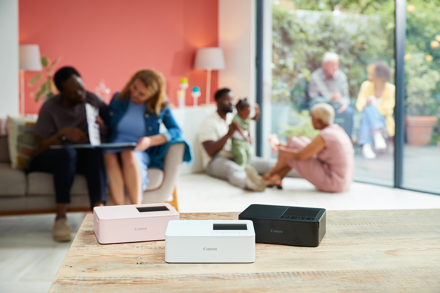 Drewniany stół z trzema drukarkami Canon. Ludzie rozmyci w tle, w tym rodzina i osoby na zewnątrz.