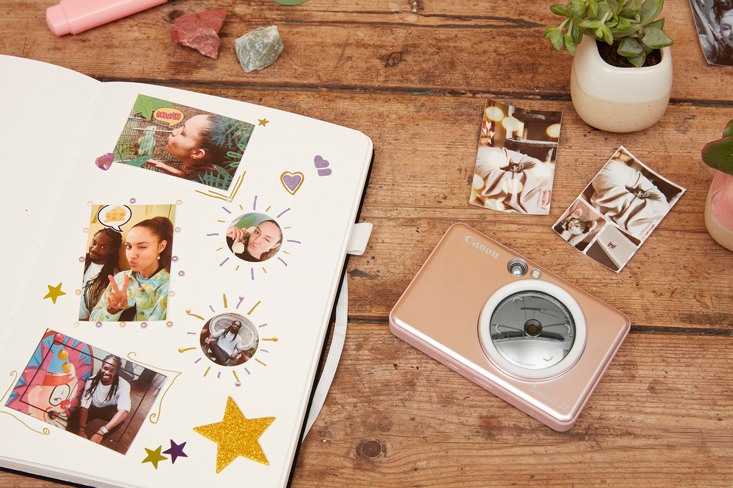 Notitieboek met foto's, stickers en een camera op een houten oppervlak. Foto's tonen mensen. Er zijn ook planten en stenen.