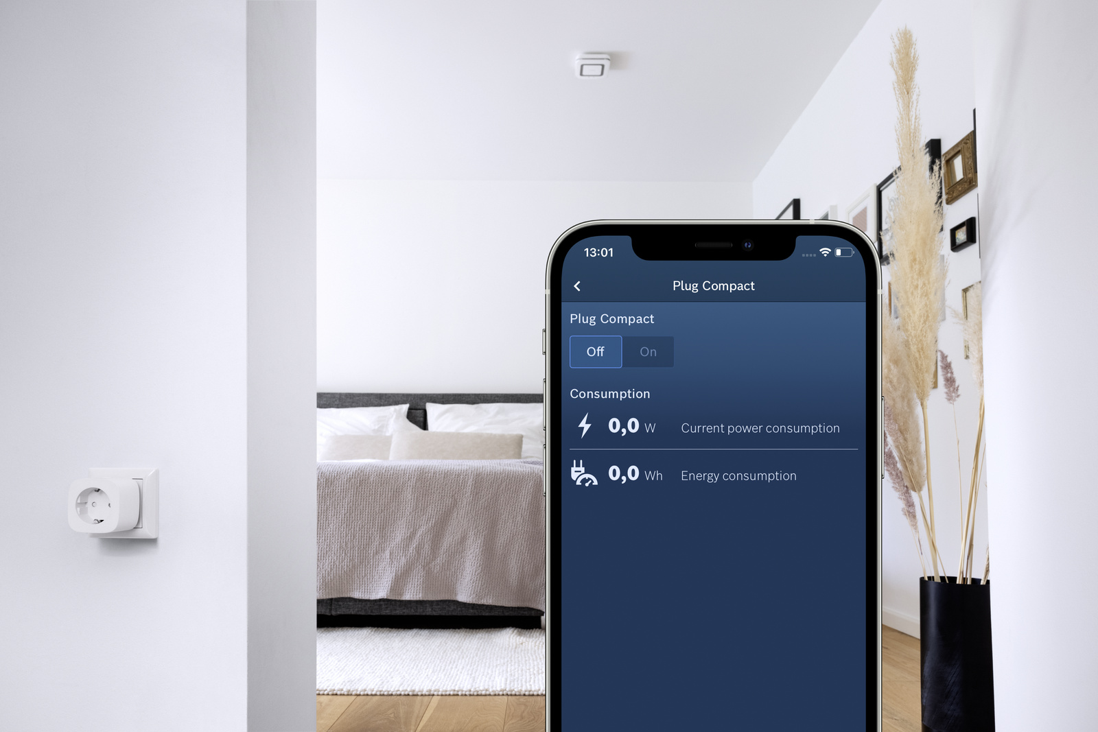 Ein Smartphone zeigt eine Smart-Plug-App. Ein weißer Stecker ist an der Wand. Ein Schlafzimmer mit Bett und Vase ist sichtbar.