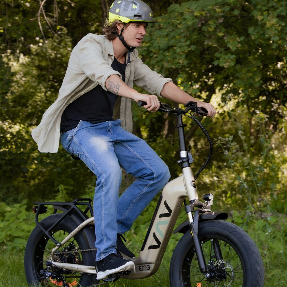 Un uomo guida una bici elettrica in un parco. Indossa un casco, jeans e una giacca. Alberi verdi sullo sfondo.