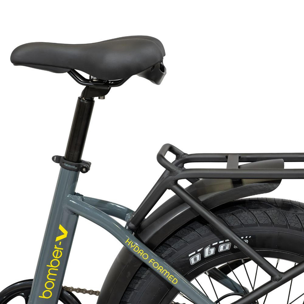 Primo piano di una bicicletta grigia con sella, portapacchi e pneumatico neri. Il testo giallo dice 'bomber-V' e 'HYDRO FORMED'.