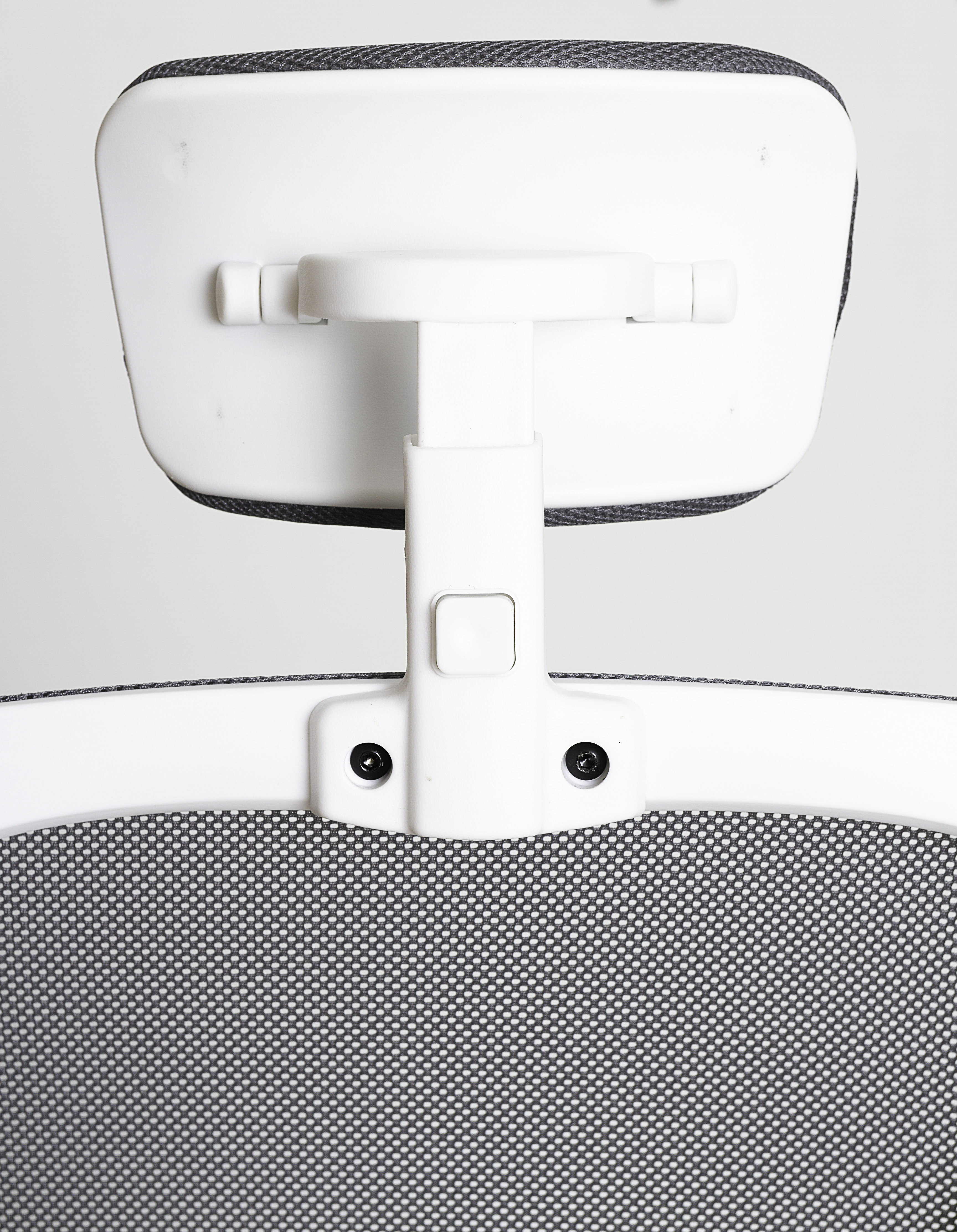 Primer plano del reposacabezas de una silla de oficina blanca. El reposacabezas tiene respaldo de malla gris y marco blanco.