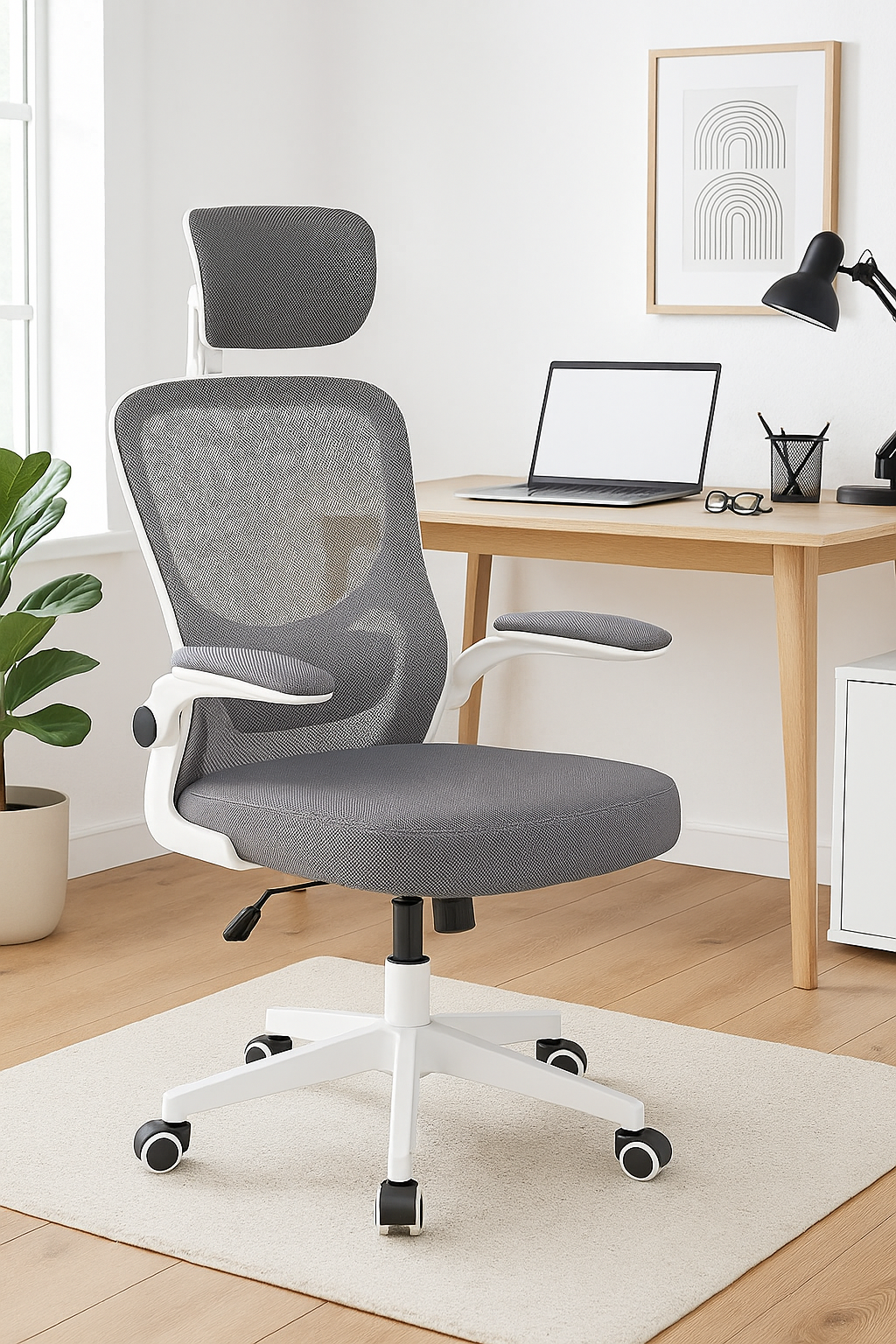 Silla de oficina gris y blanca frente a un escritorio con portátil, lámpara y obra de arte. Una planta a la izquierda.