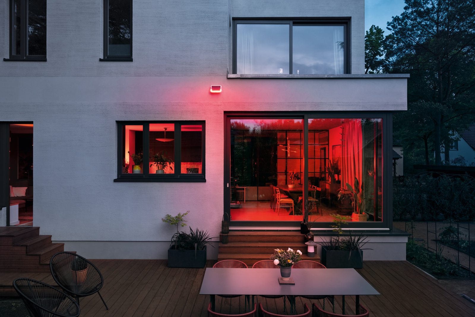 Außenansicht eines modernen Hauses bei Dämmerung, mit roter Innenbeleuchtung durch Fenster und Schiebetüren.