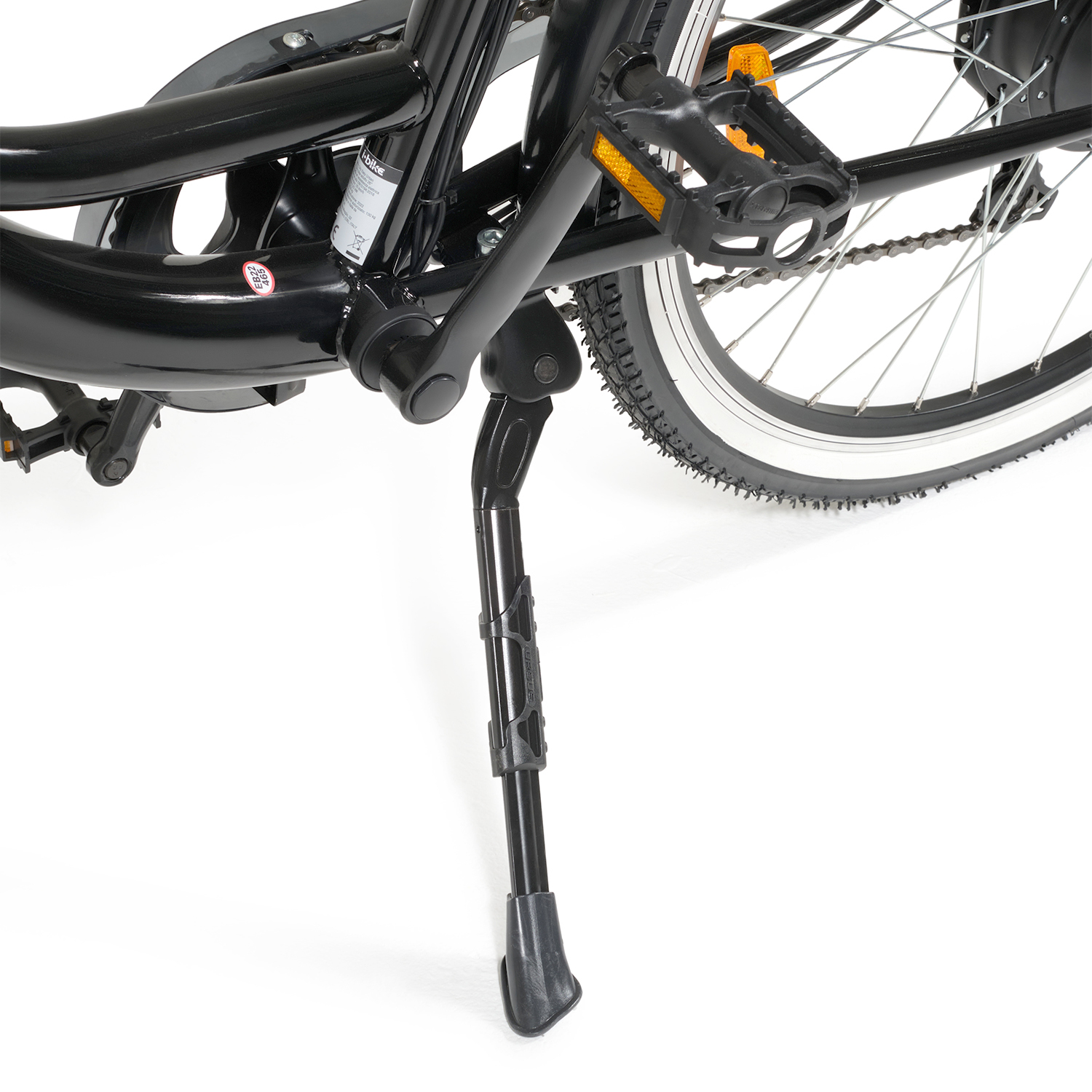 Primo piano di una bicicletta nera con cavalletto. Parti visibili: telaio, pedali, ruota, catena e pneumatici. Sfondo bianco.