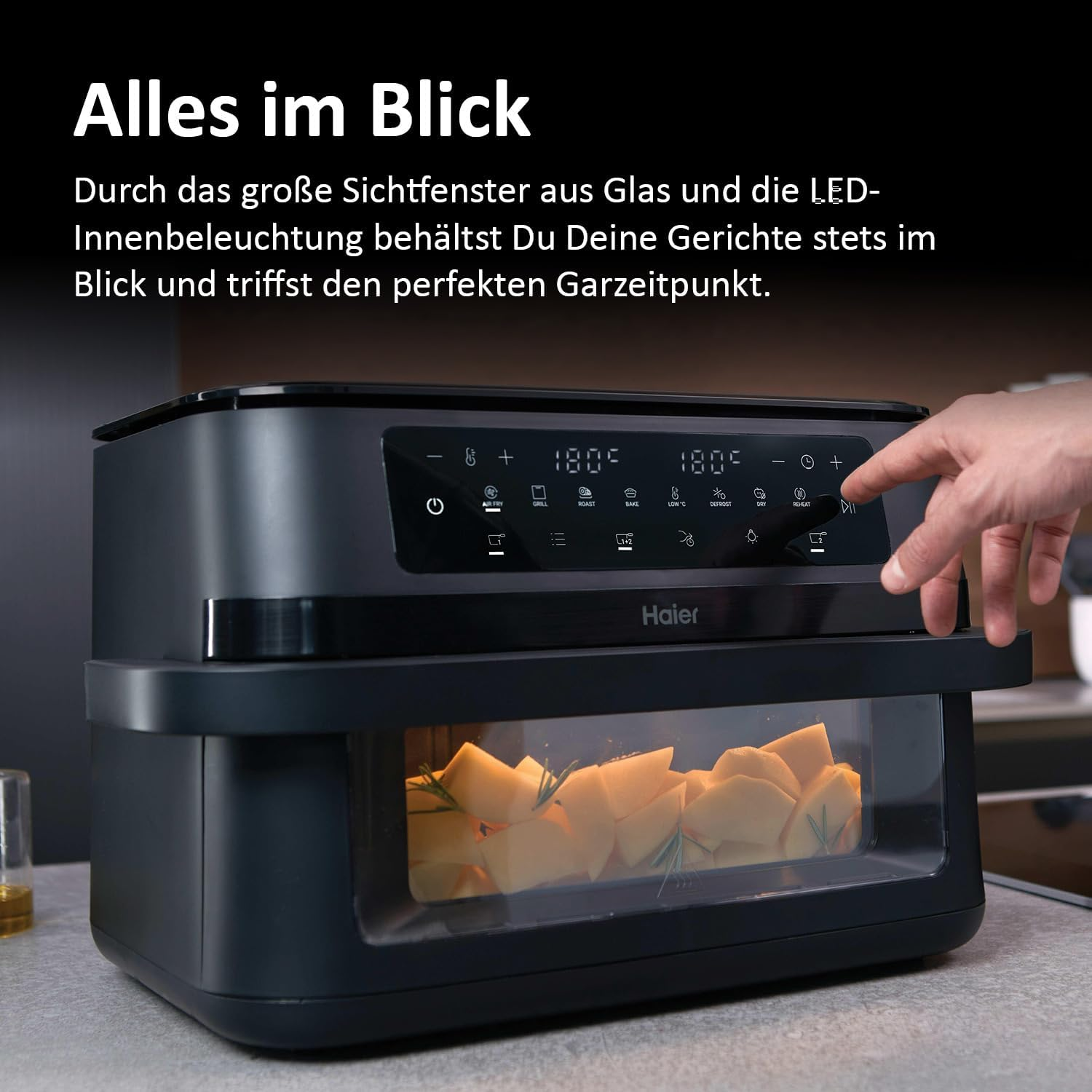 Ein schwarzer Haier-Ofen mit sichtbarem Essen. Eine Hand berührt das Bedienfeld. Der Hintergrund ist unscharf.