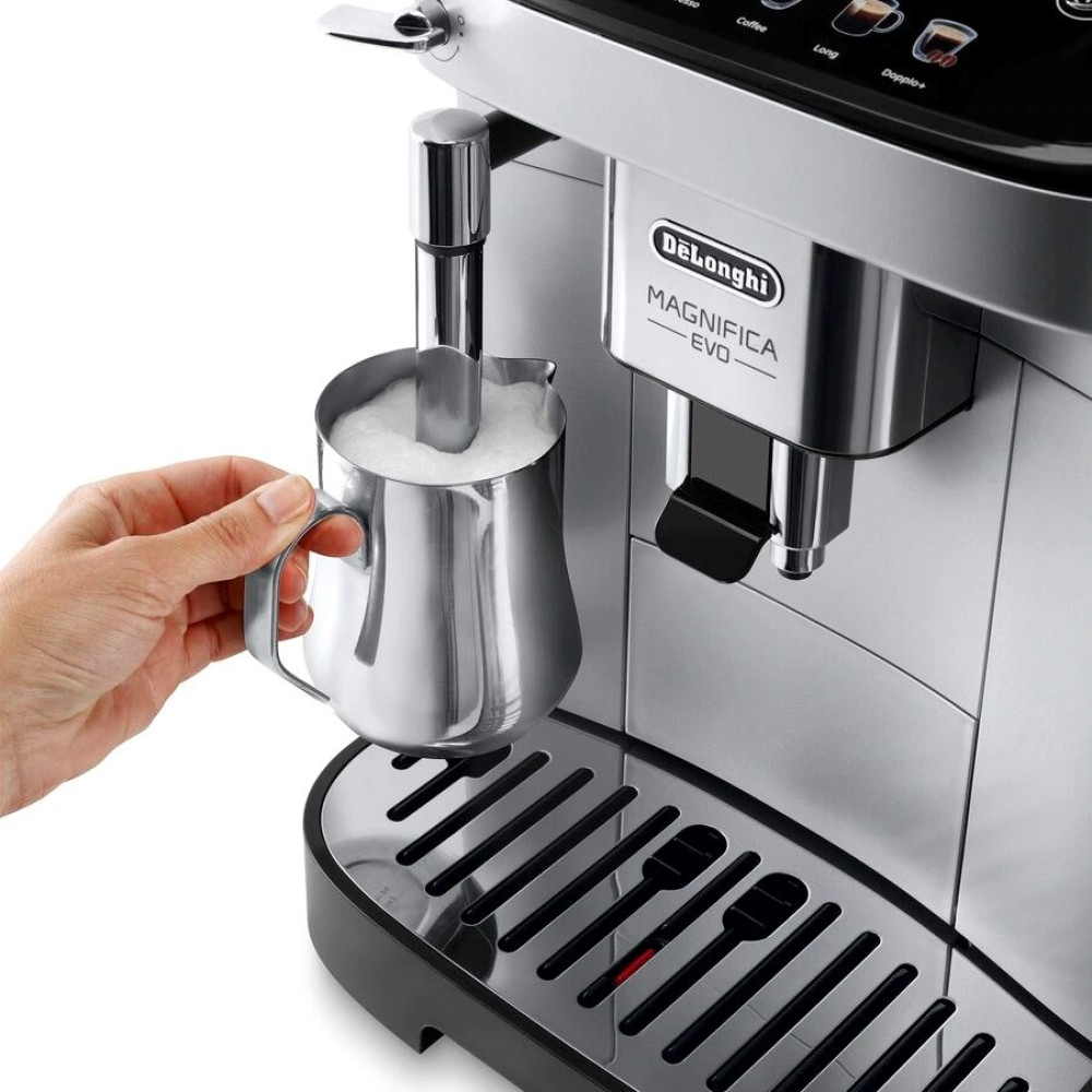 Ręka trzyma srebrny dzbanek do spieniania mleka w pobliżu ekspresu do kawy Delonghi Magnifica Evo.