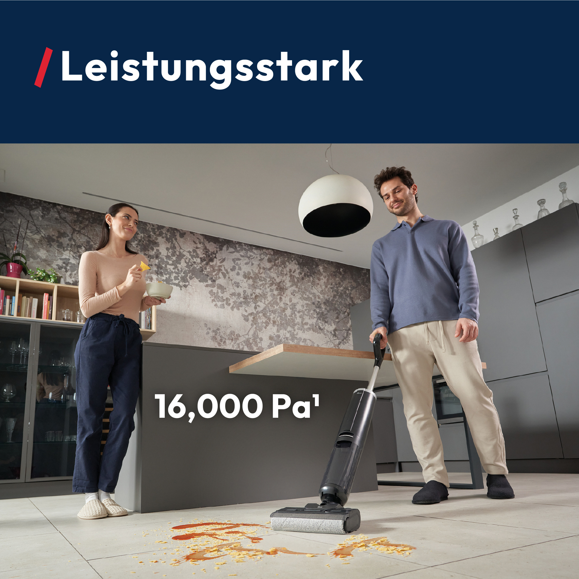 Un homme utilise un aspirateur sur un dégât alimentaire. Une femme tient un bol. Cadre de cuisine.