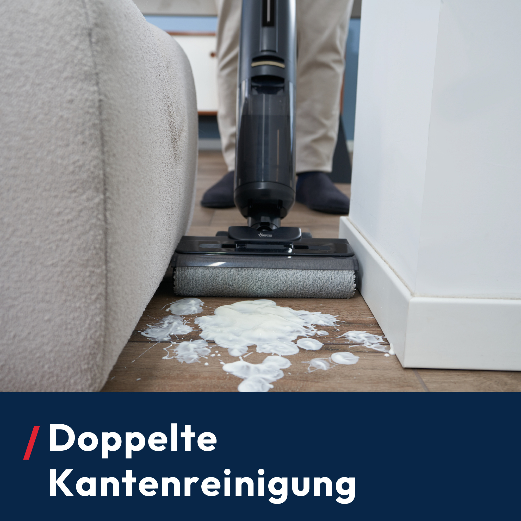 Une personne aspire du liquide blanc renversé sur un plancher en bois près d'un canapé et d'un mur, à l'aide d'un aspirateur noir.