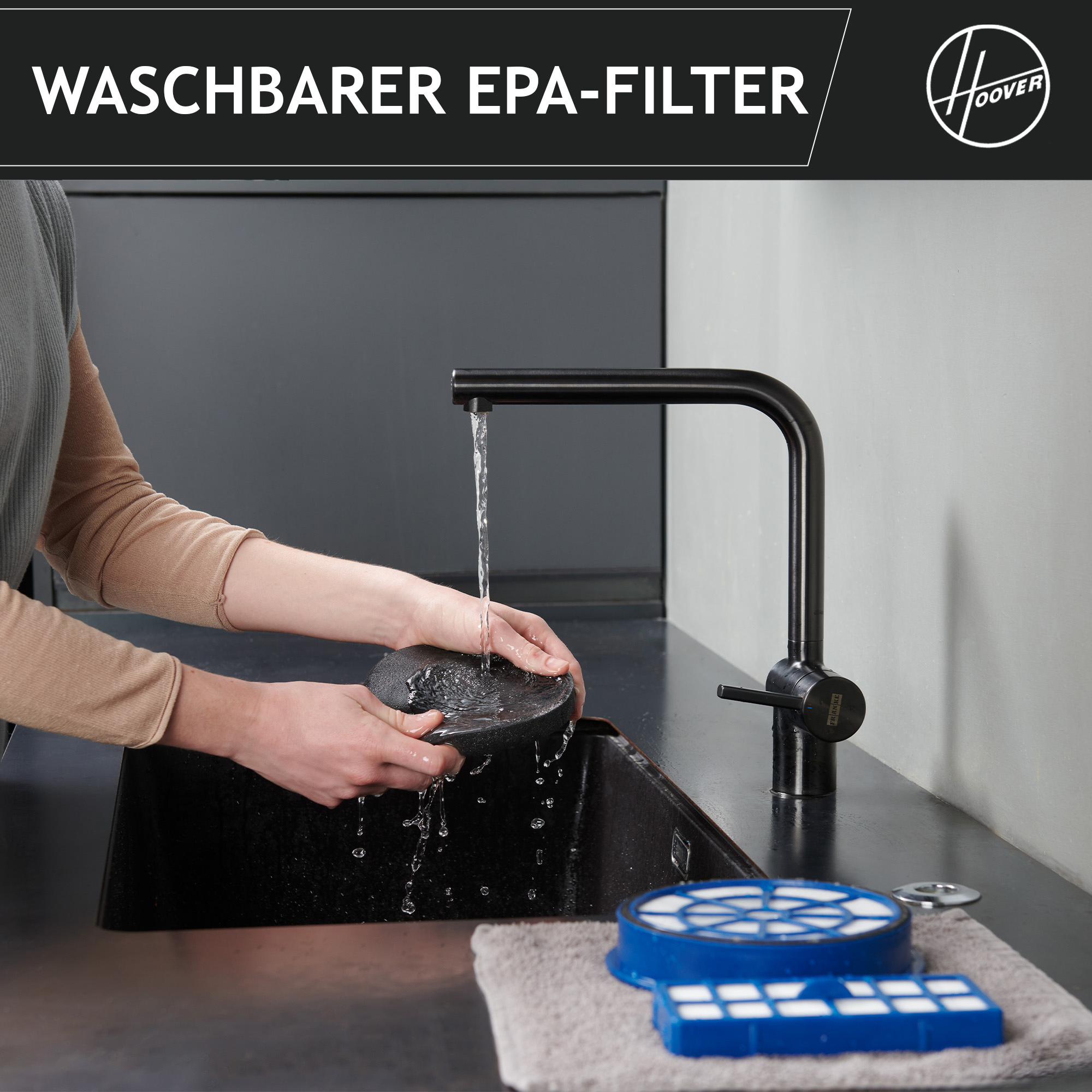 Eine Person wäscht einen EPA-Filter unter einem schwarzen Wasserhahn. Ein blauer Filter und ein Handtuch liegen auf der Theke.