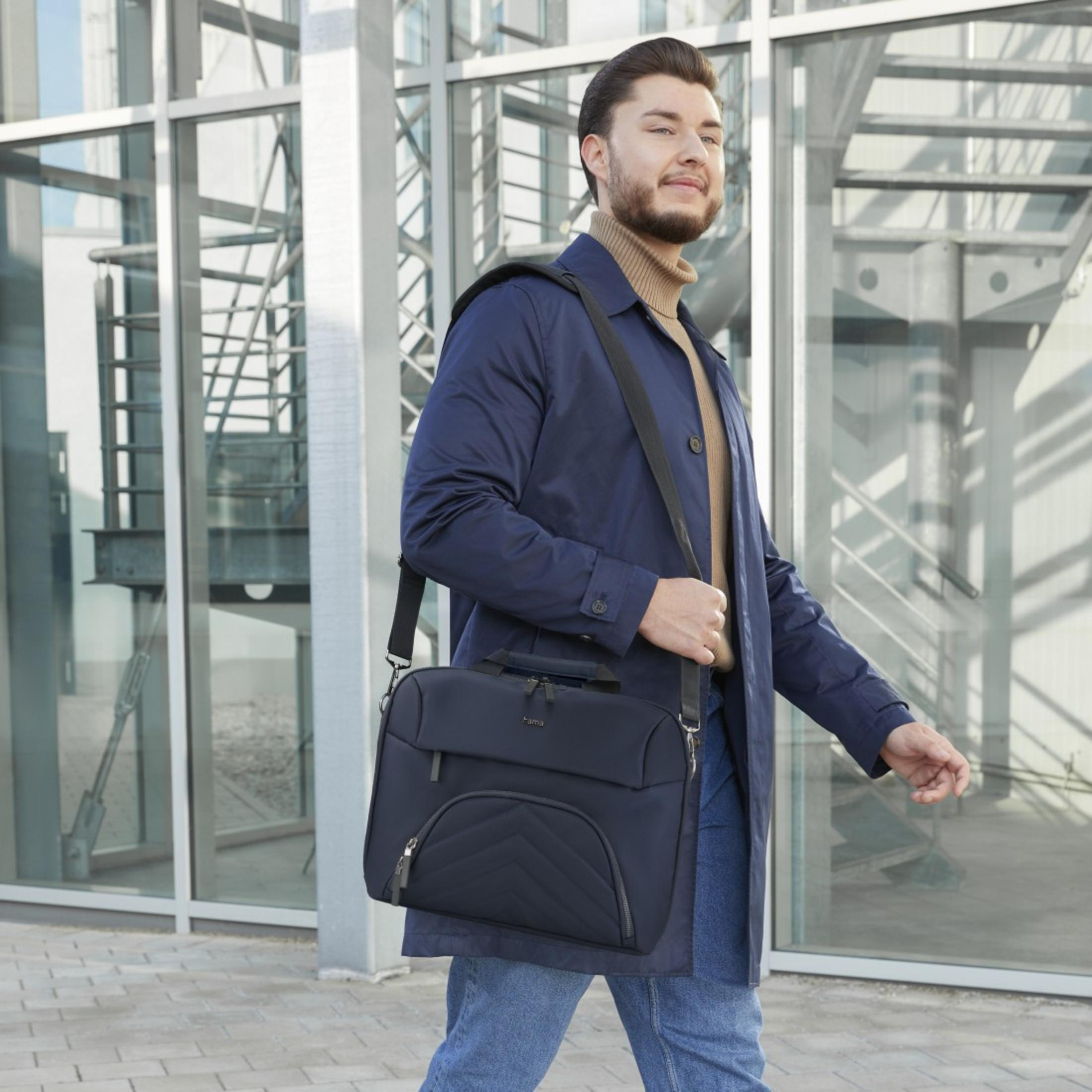 Mężczyzna w niebieskim płaszczu, z torbą, idzie. W tle szklany budynek.