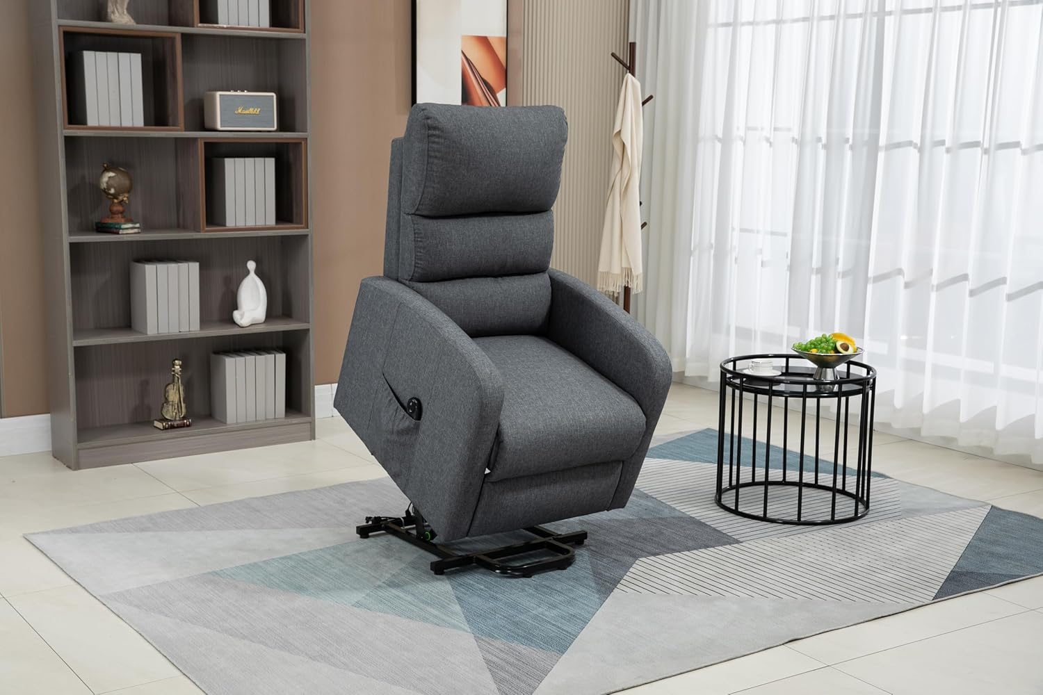 Un sillón reclinable gris en una sala de estar. Una pequeña mesa negra con un frutero. Una estantería a la izquierda.