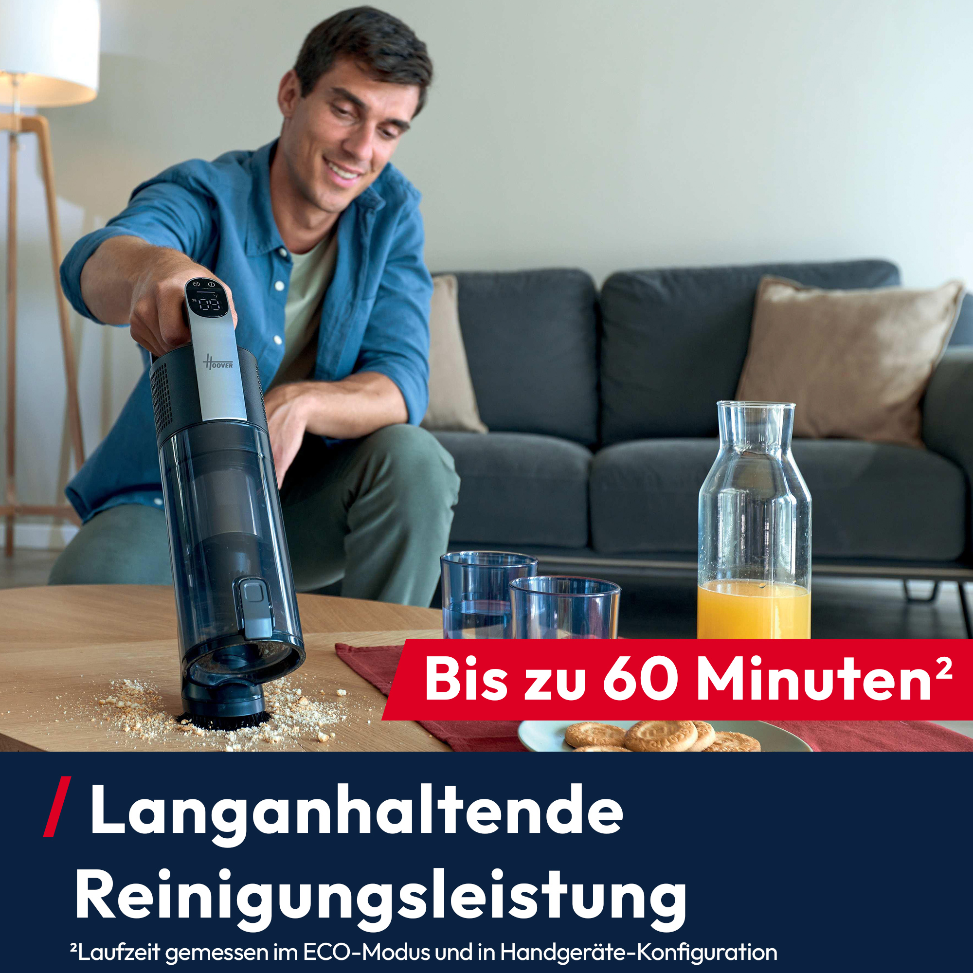 Ein Mann benutzt einen Staubsauger auf einem Tisch mit Krümeln. Ein Sofa, Gläser, Saft und Kekse sind ebenfalls zu sehen.