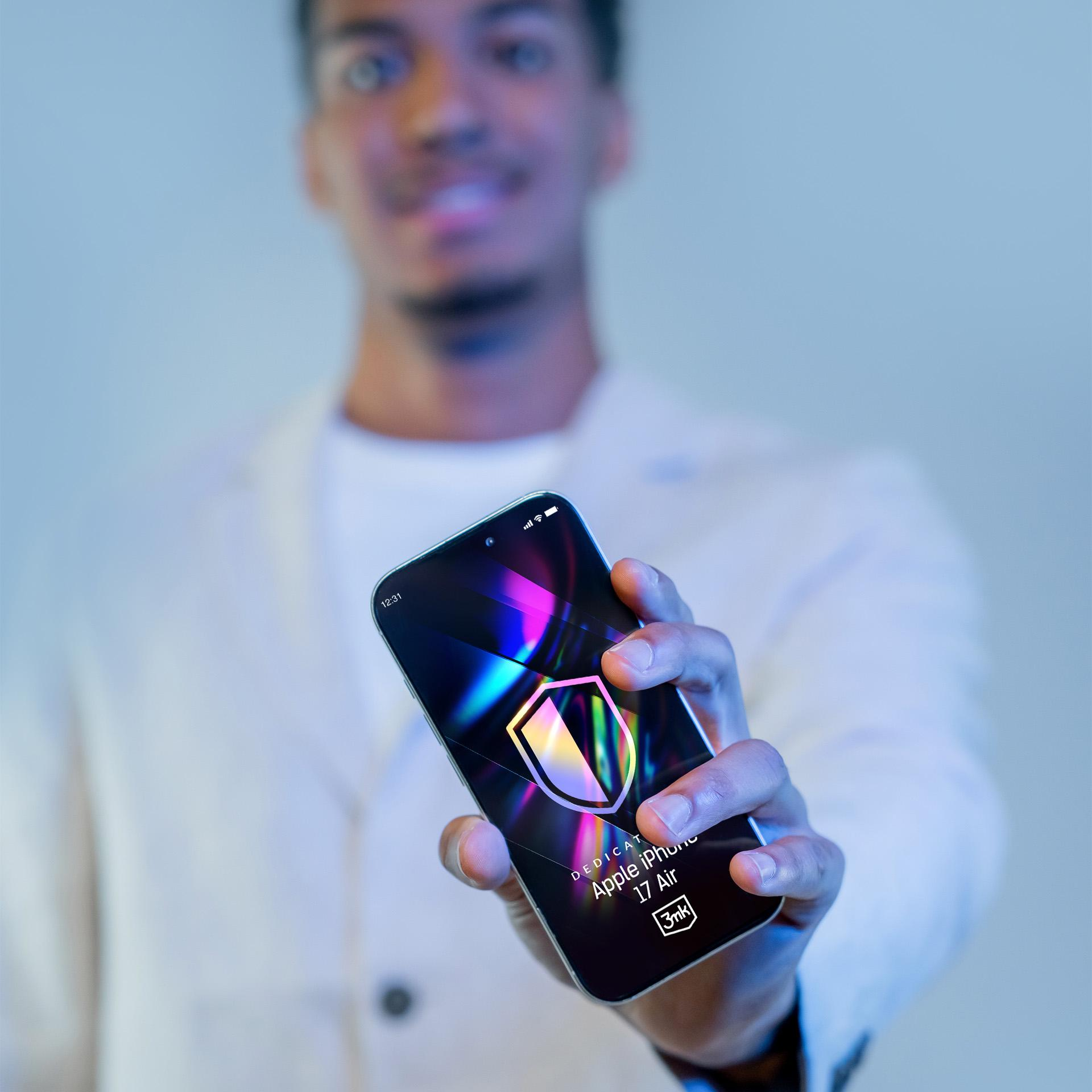 Uomo che tiene in mano un telefono con un logo a scudo. Lo schermo dice 'Apple iPhone 17 Air'. L'uomo indossa una giacca bianca.