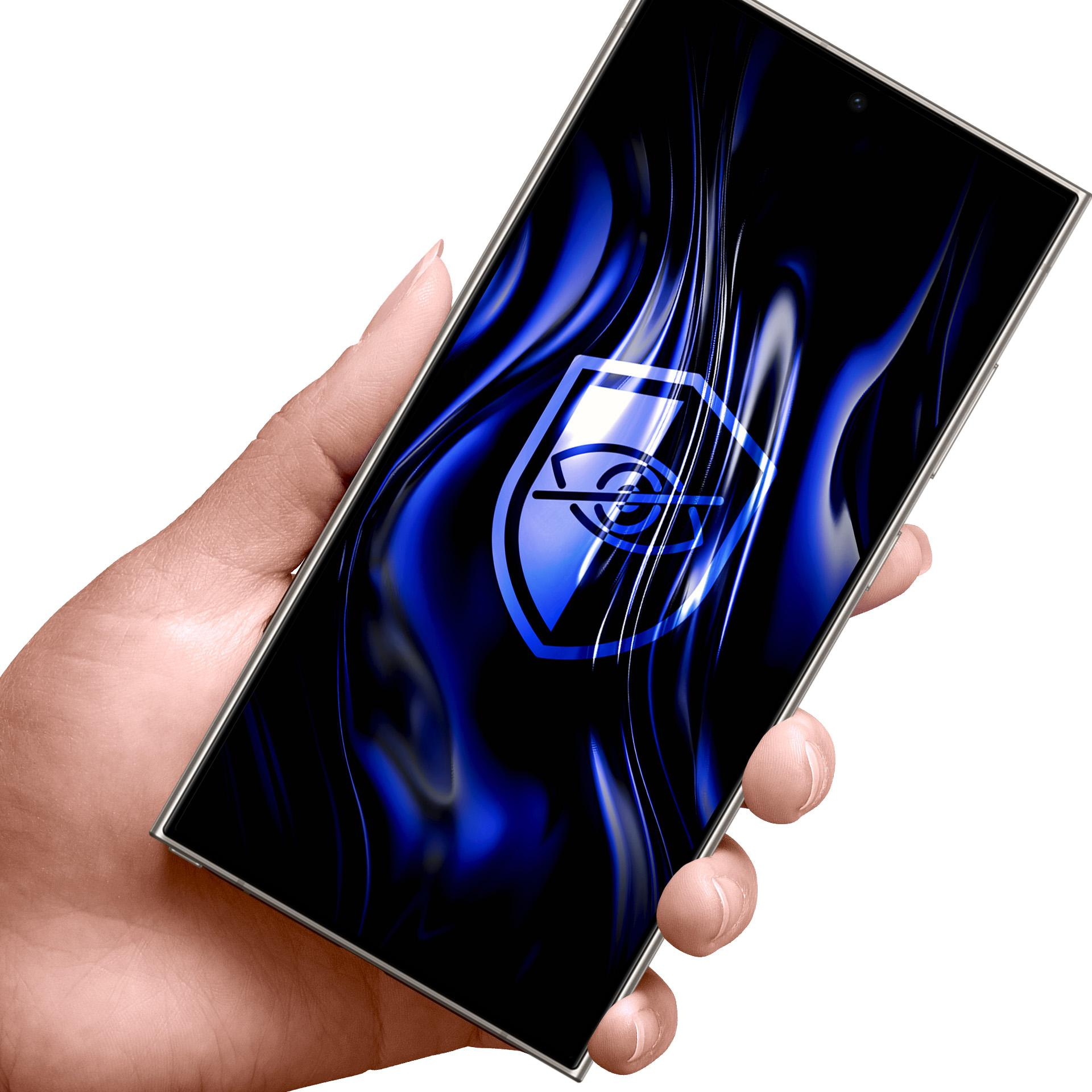 Ręka trzyma smartfon z niebieskim logo tarczy na ekranie.