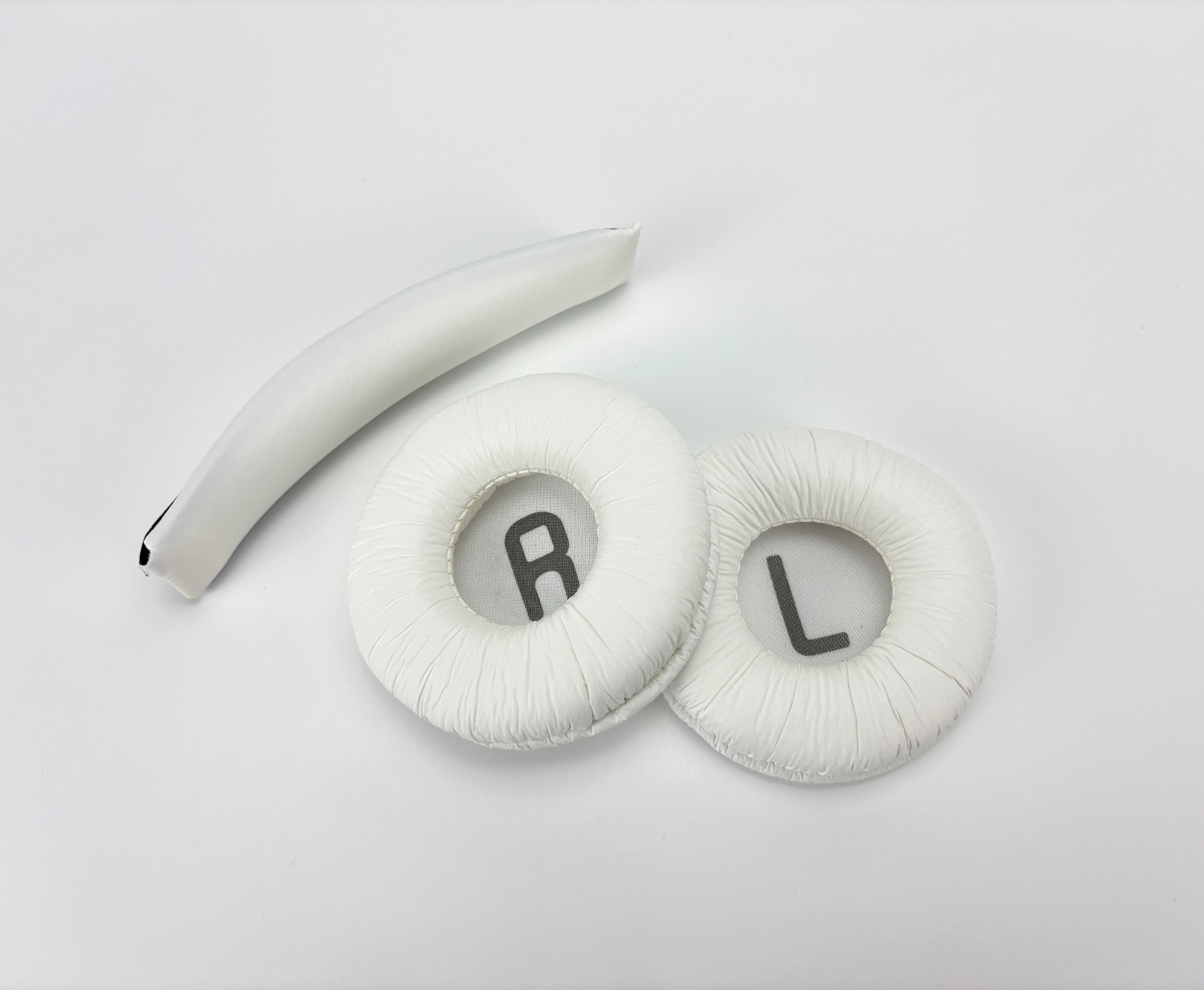 Białe części słuchawek na białej powierzchni. Zawiera nauszniki, poduszkę pałąka. Widoczne 'R' i 'L'.