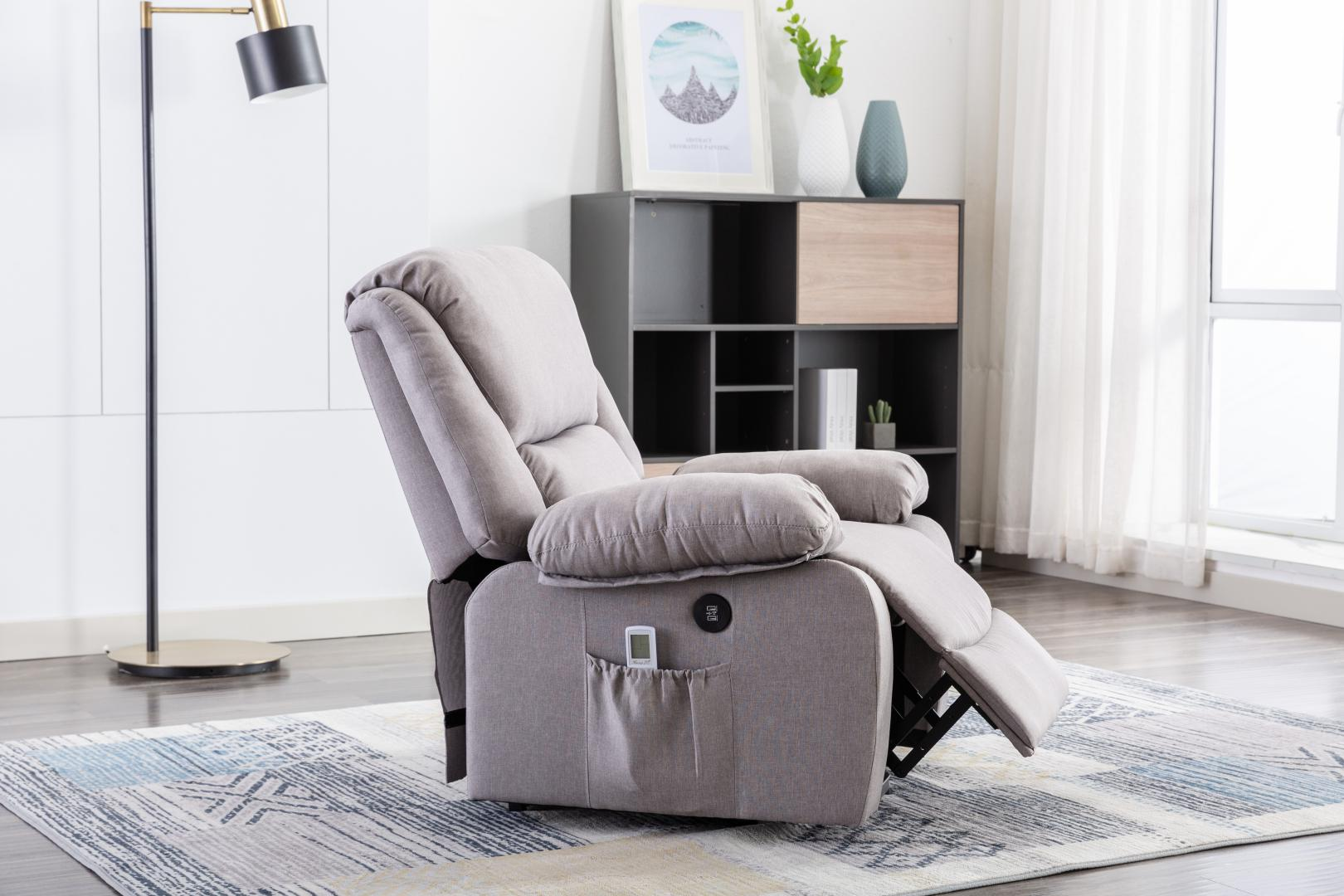 Un sillón reclinable gris en una sala de estar. Hay una lámpara de pie, un gabinete con decoración y una ventana con cortinas.