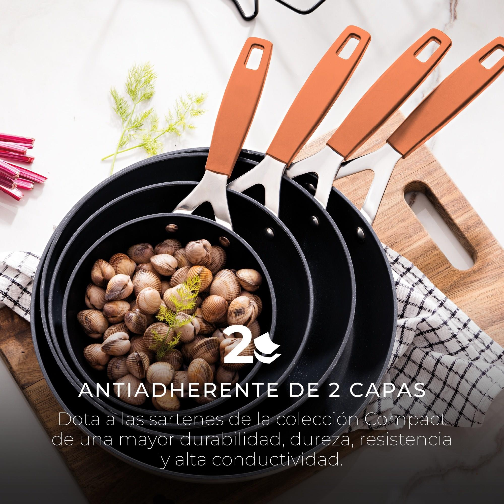 Juego de sartenes negras con mangos naranjas, llenas de almejas. Sobre una tabla de madera, con hierbas y un paño a cuadros.