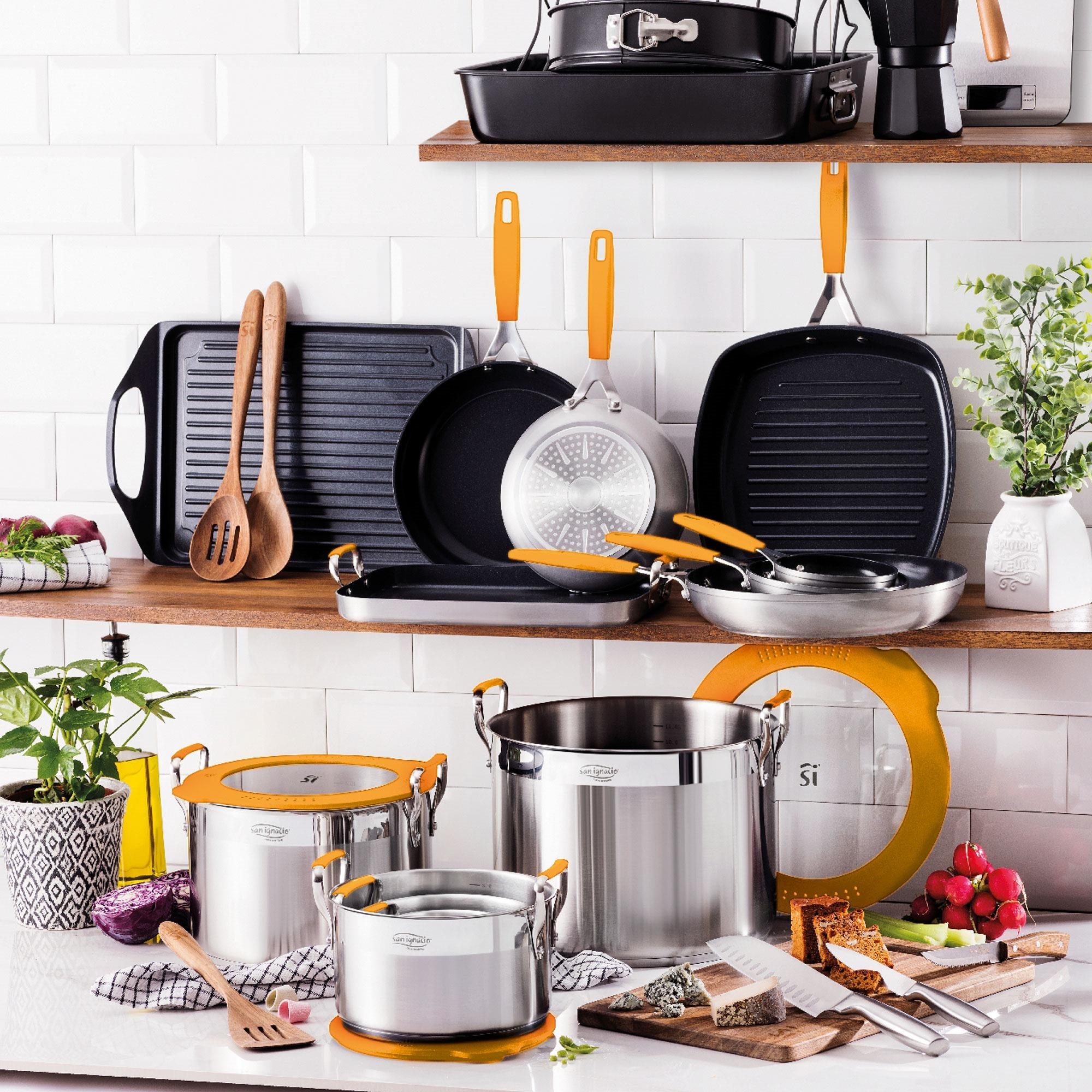 Escena de cocina con utensilios de cocina de acero inoxidable. Sartenes, ollas y tablas de cortar con alimentos. Fondo de azulejos blancos.