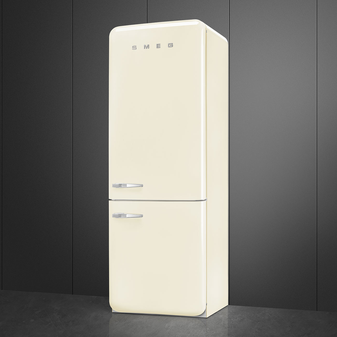 Un refrigerador SMEG crema está contra una pared gris oscuro. Tiene dos puertas y manijas cromadas. El piso es gris.
