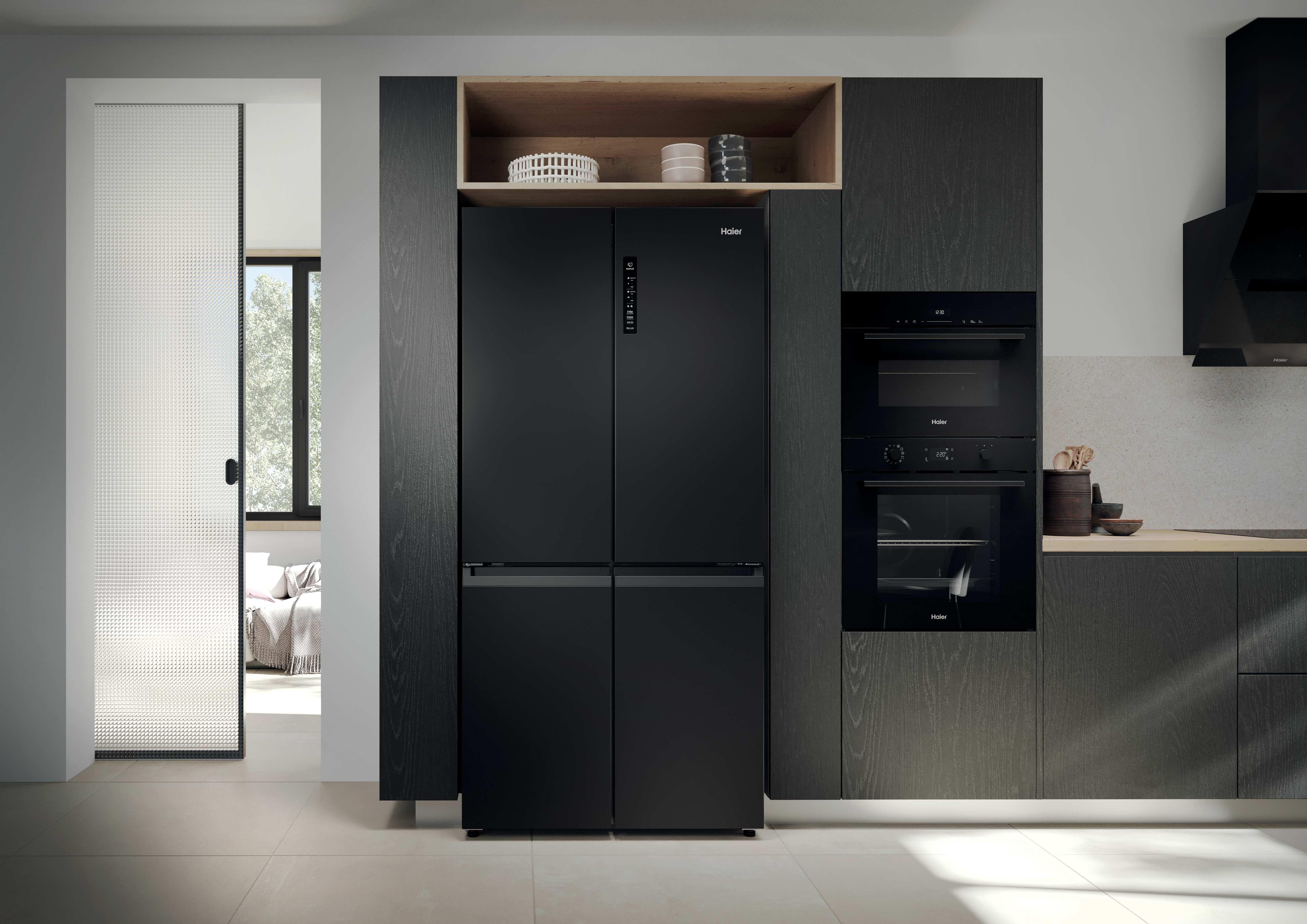 Cucina moderna con frigorifero nero, forni e pavimento chiaro. Una porta a vetri è a sinistra.