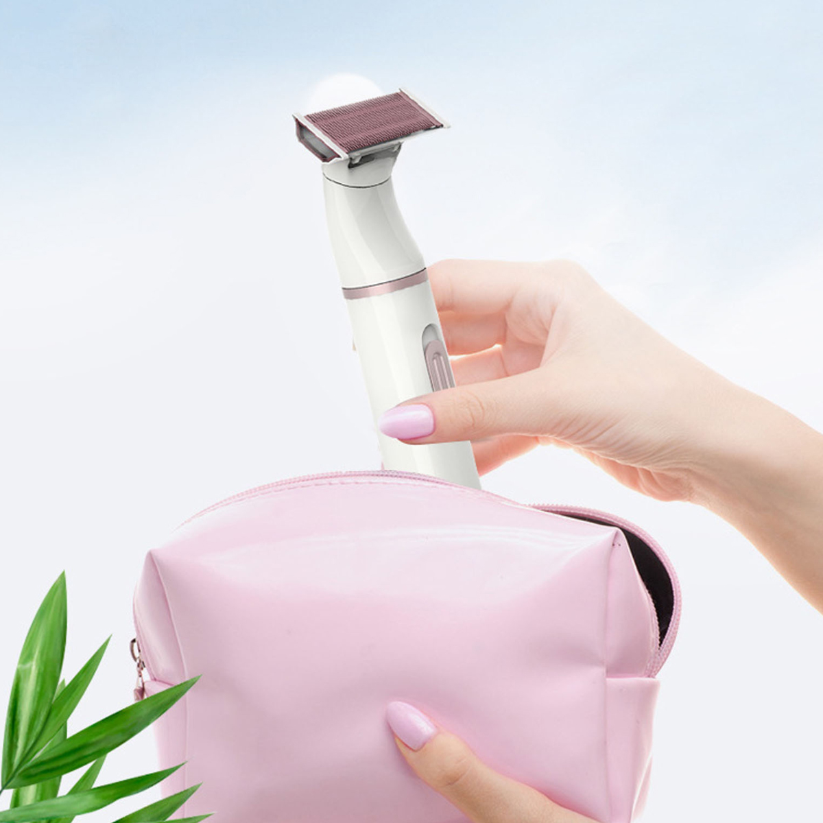 Eine Hand hält einen weißen und roségoldenen Rasierer und legt ihn in eine rosa Kosmetiktasche. Grüne Blätter sind im Vordergrund.