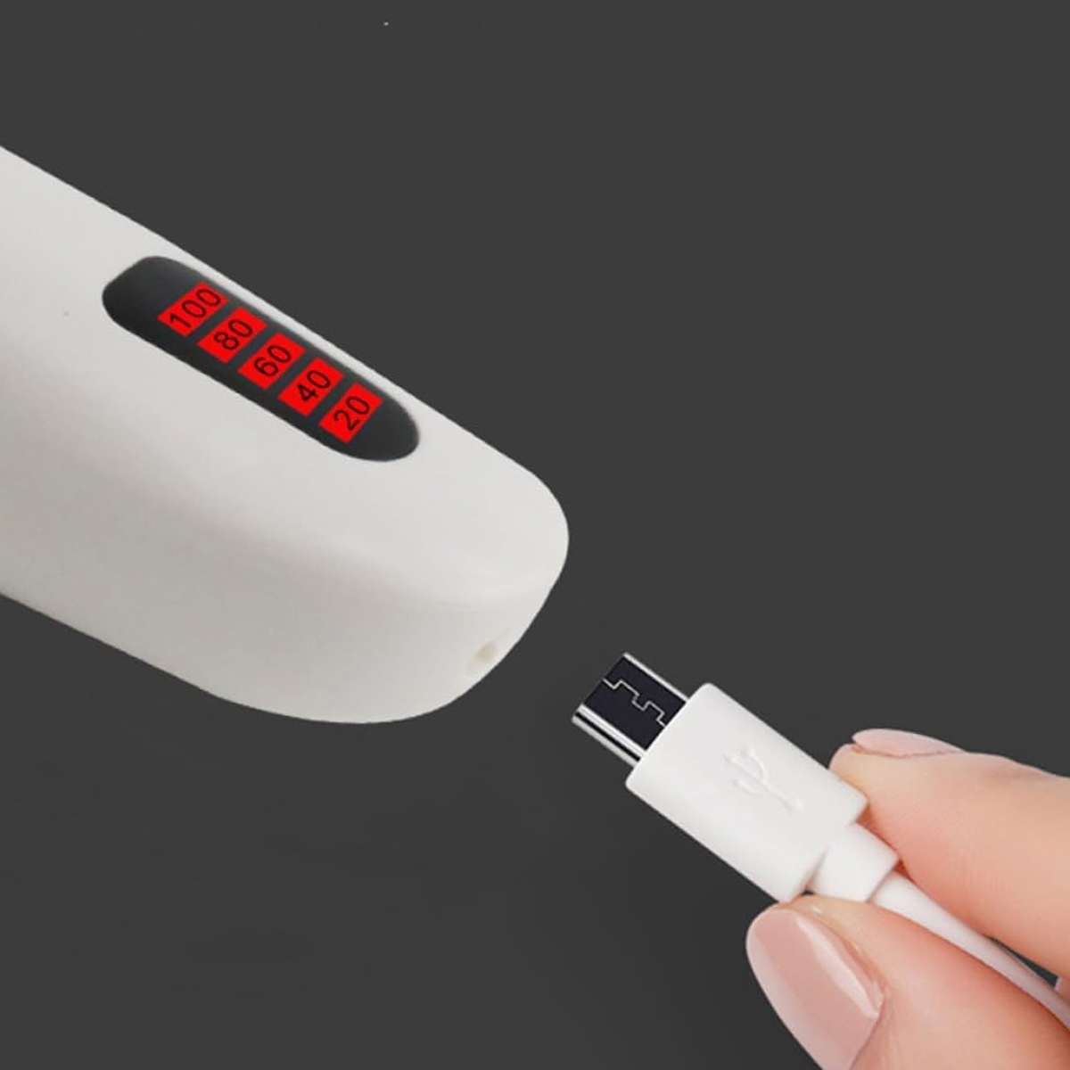 Ein weißes Gerät zeigt den Akkustand an. Eine Hand hält ein weißes USB-Kabel, das angeschlossen werden soll. Dunkelgrauer Hintergrund.